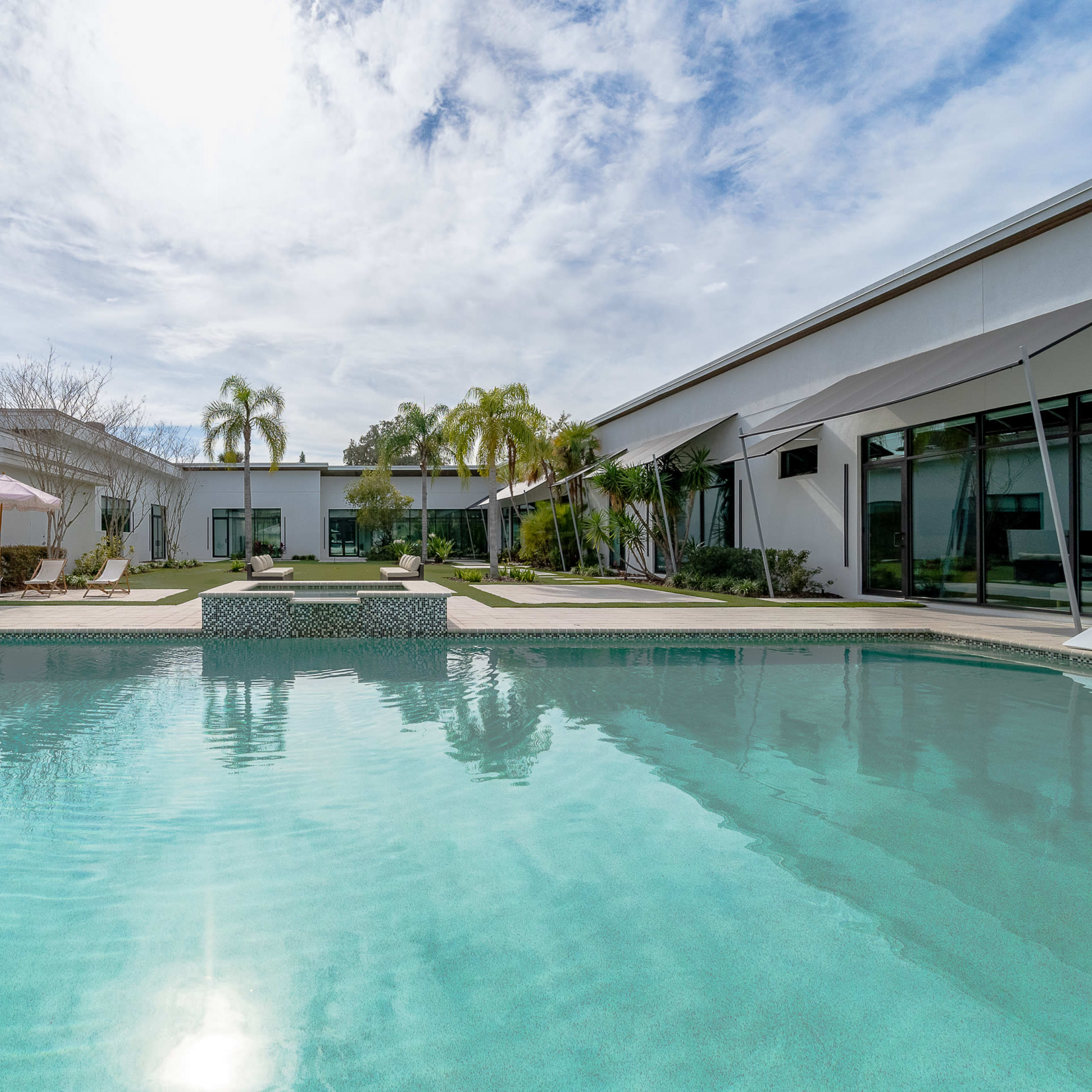 A modern house with a pool in the foreground, surrounded by palm trees and landscaped gardens.