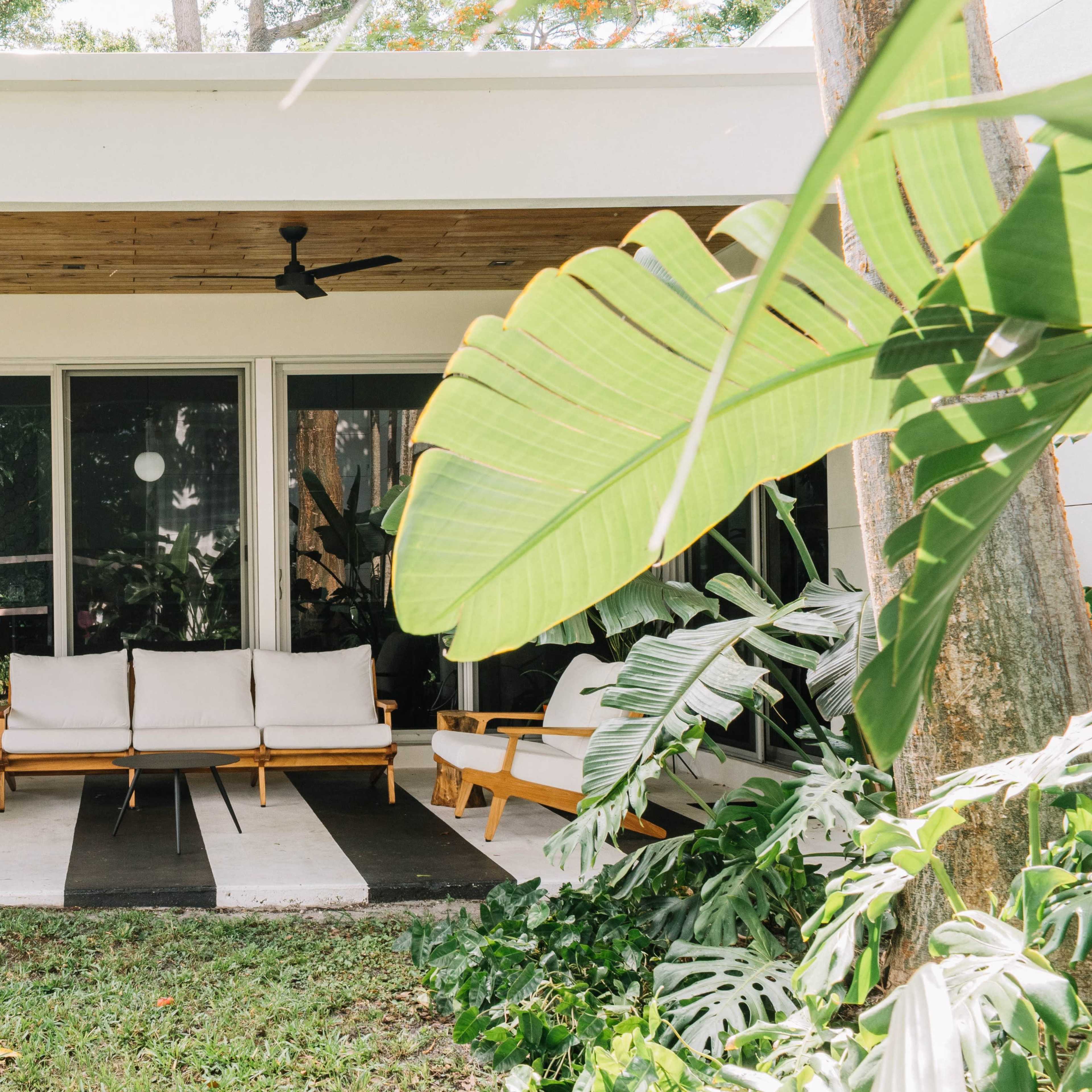 A modern patio features wooden furniture arranged on a striped floor, surrounded by greenery.