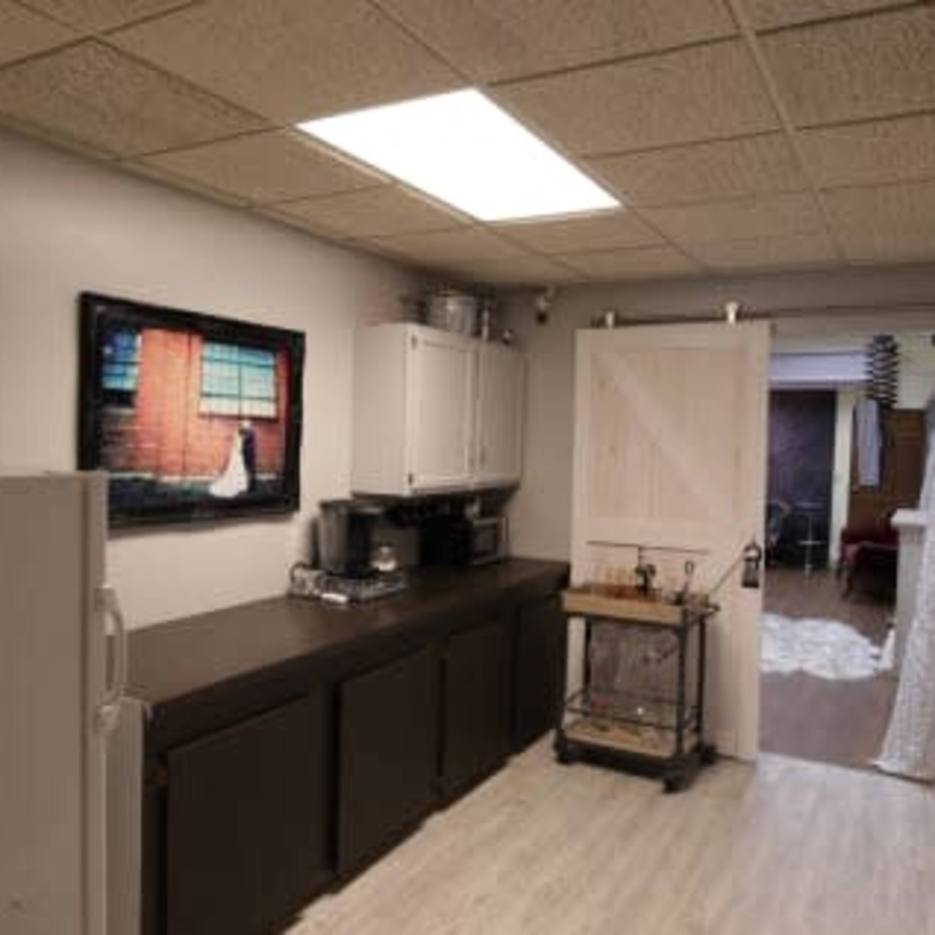 A kitchen with a refrigerator, a long black countertop, a white cabinet, and a door leading to another room.