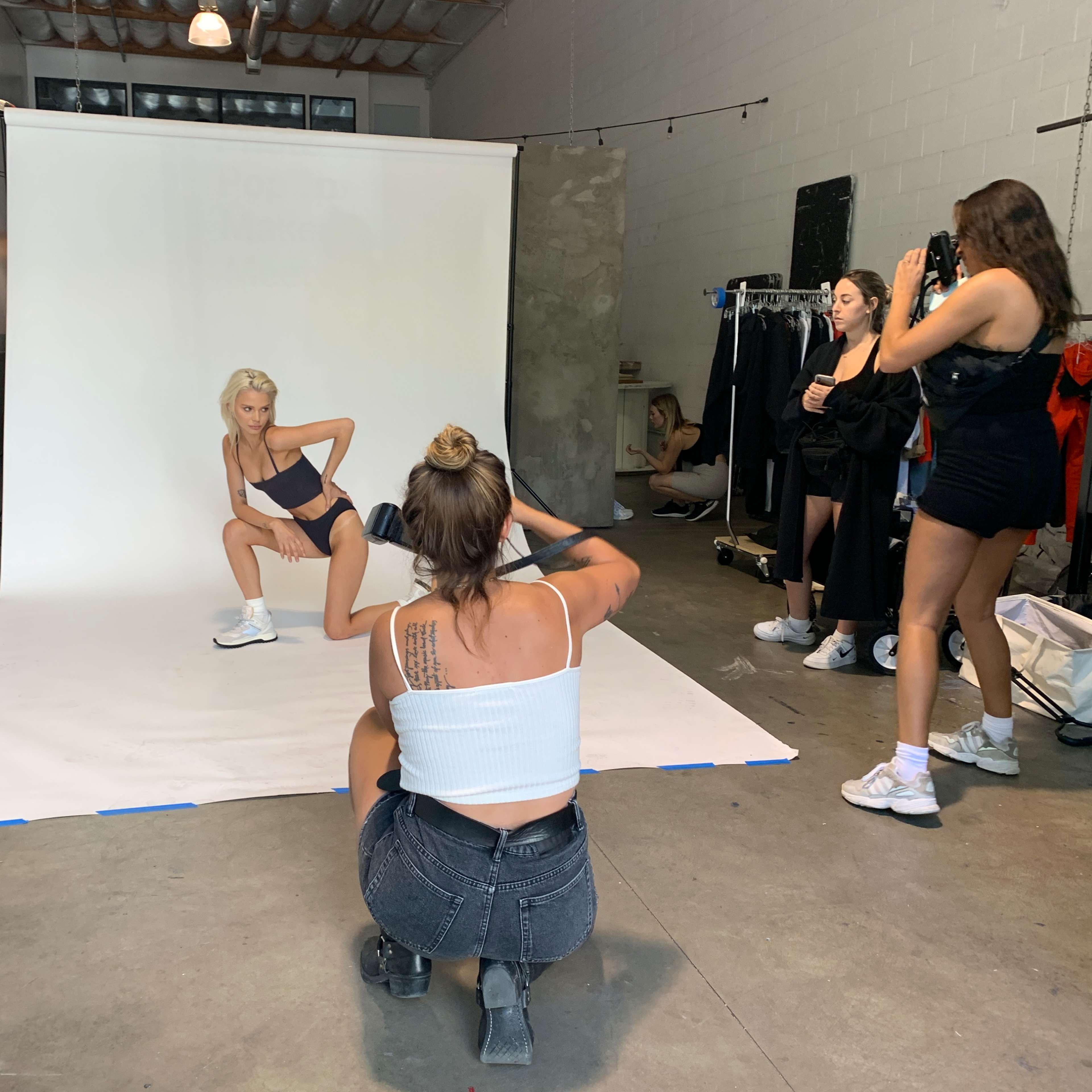A model poses on a white backdrop while photographers and assistants work in a studio setting.