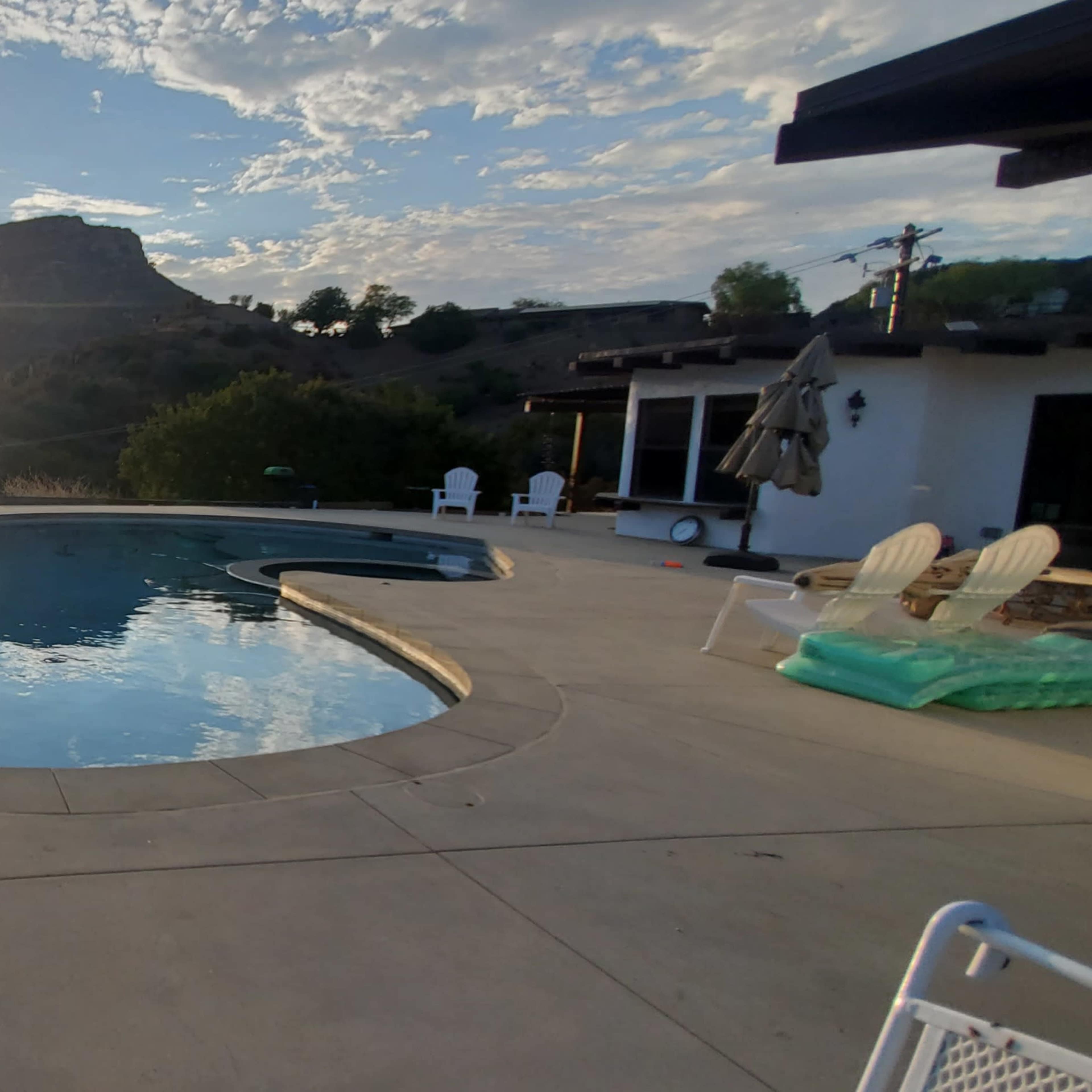 A circular swimming pool at sunset with a mountain silhouette in the background and outdoor seating nearby.