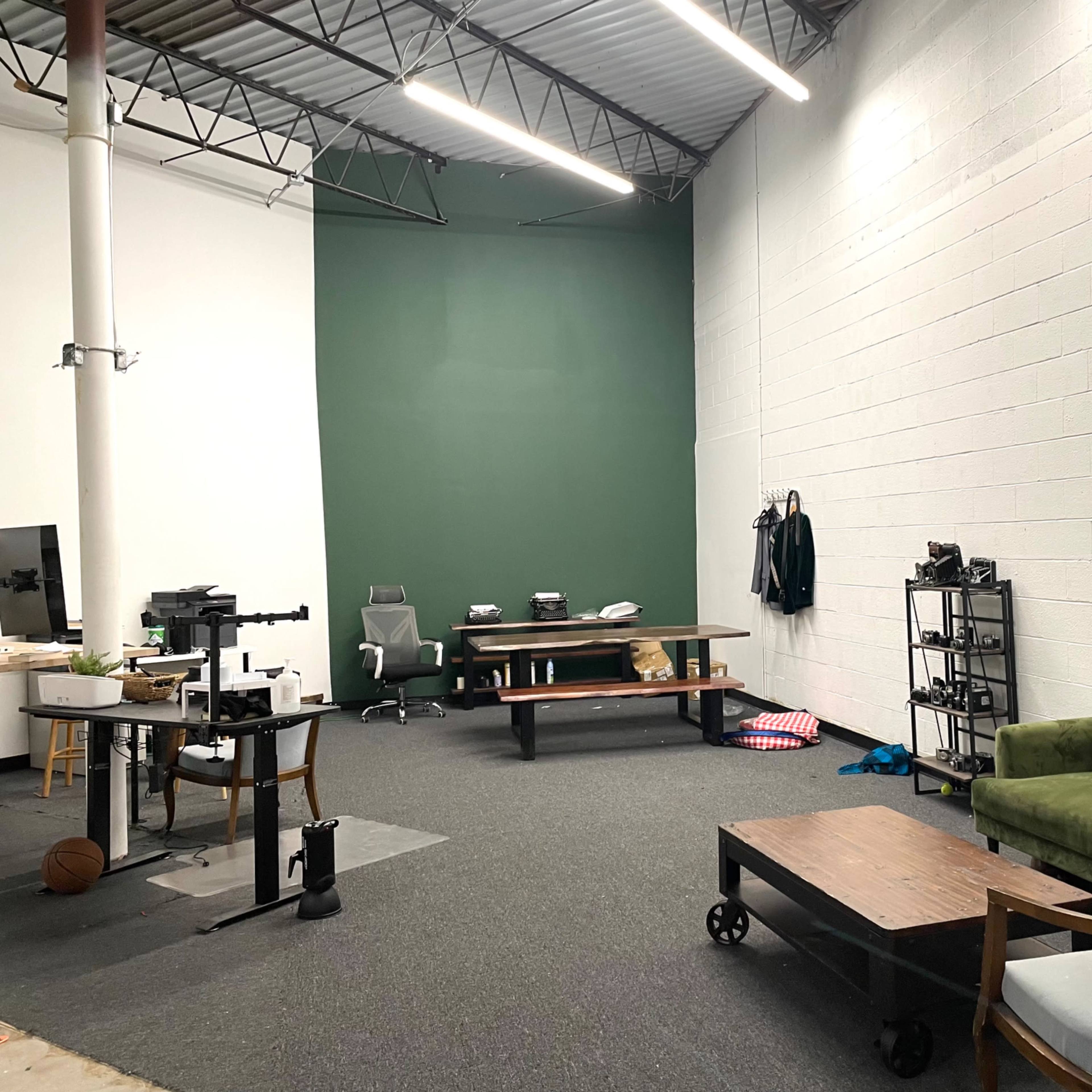 A spacious, well-lit office with a green accent wall, featuring a green couch, a wooden table, and various office furniture.