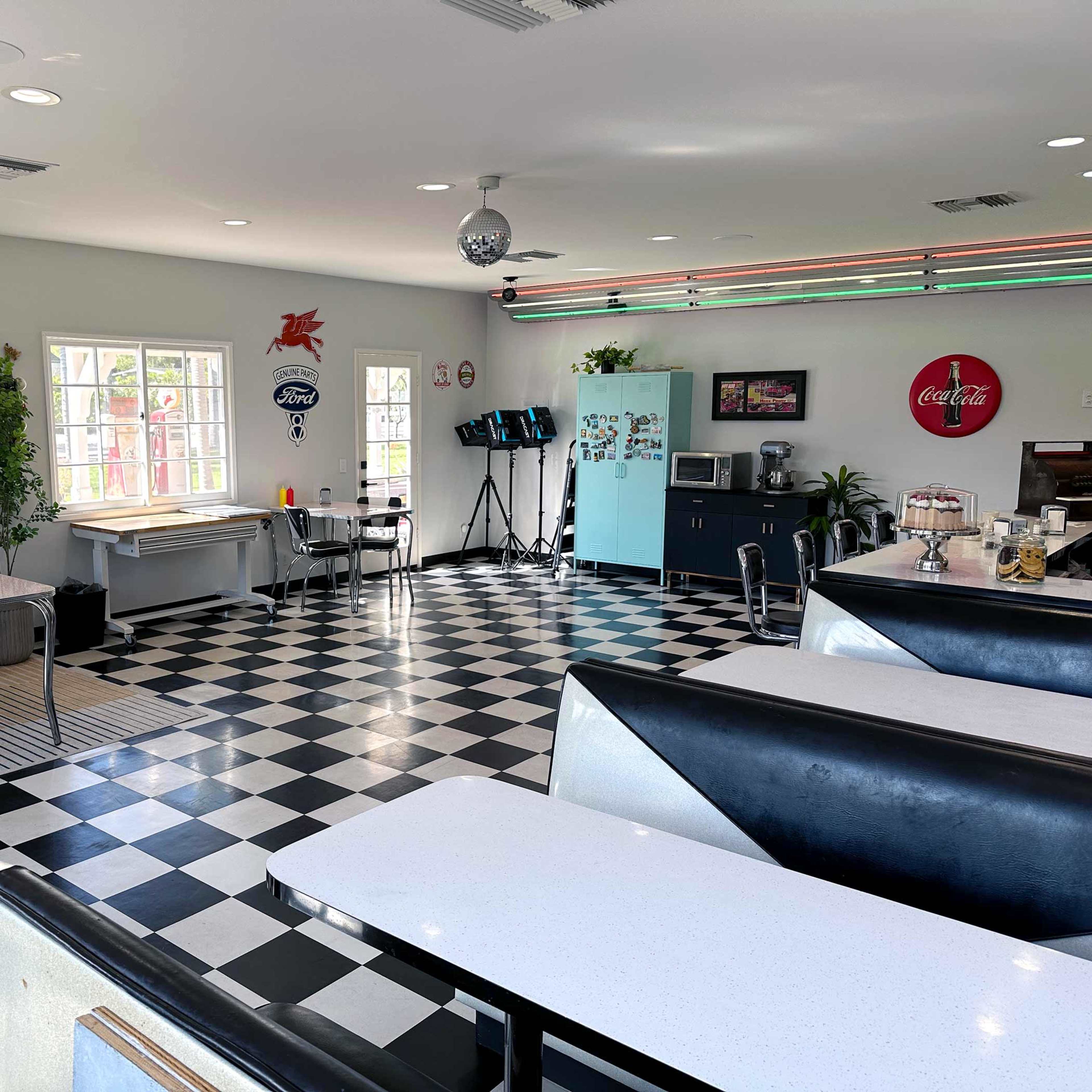 A vintage-style diner interior with black and white checkered flooring, booths, a small dining area, and retro decor.