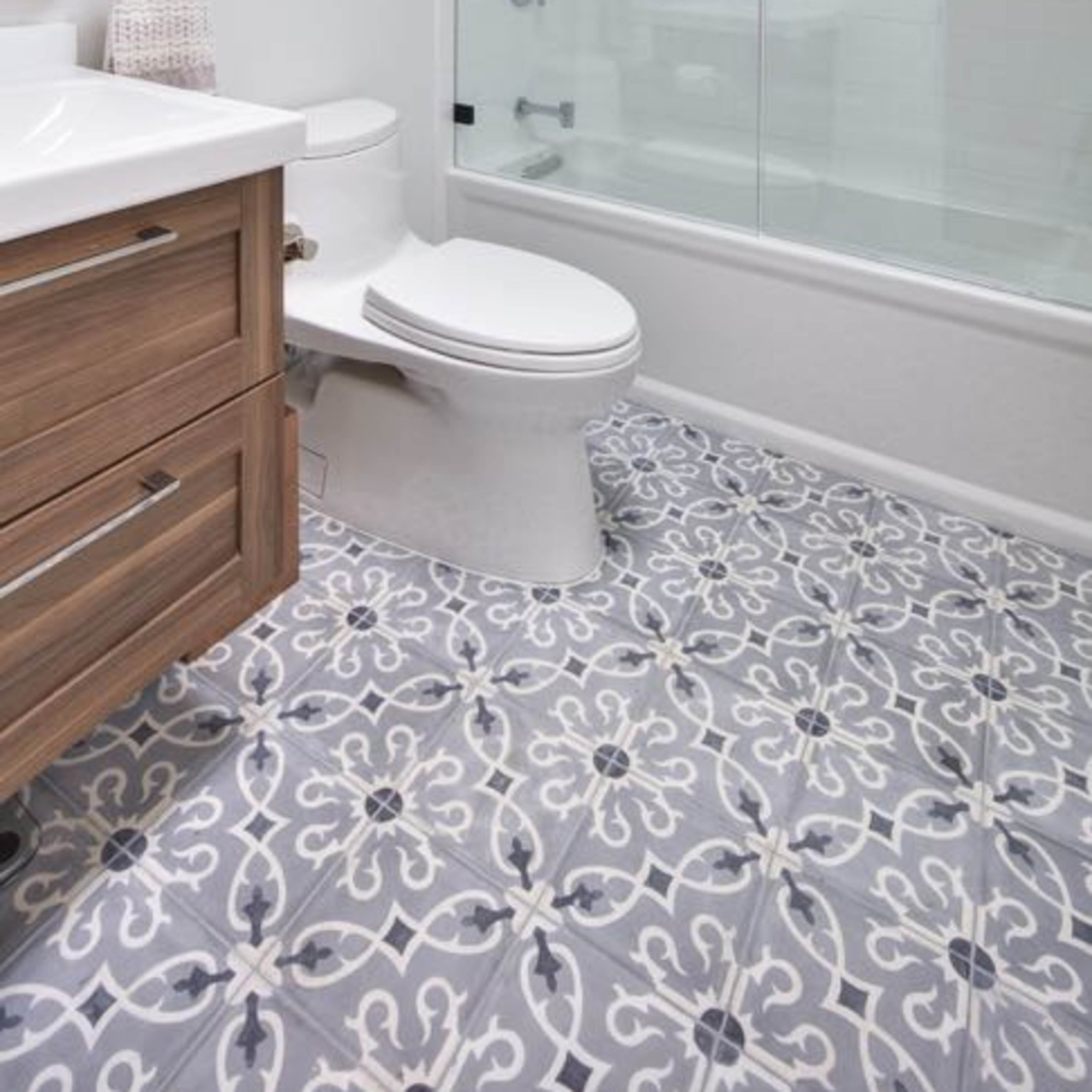 A modern bathroom featuring a glass shower enclosure, a white toilet, and patterned tile flooring.