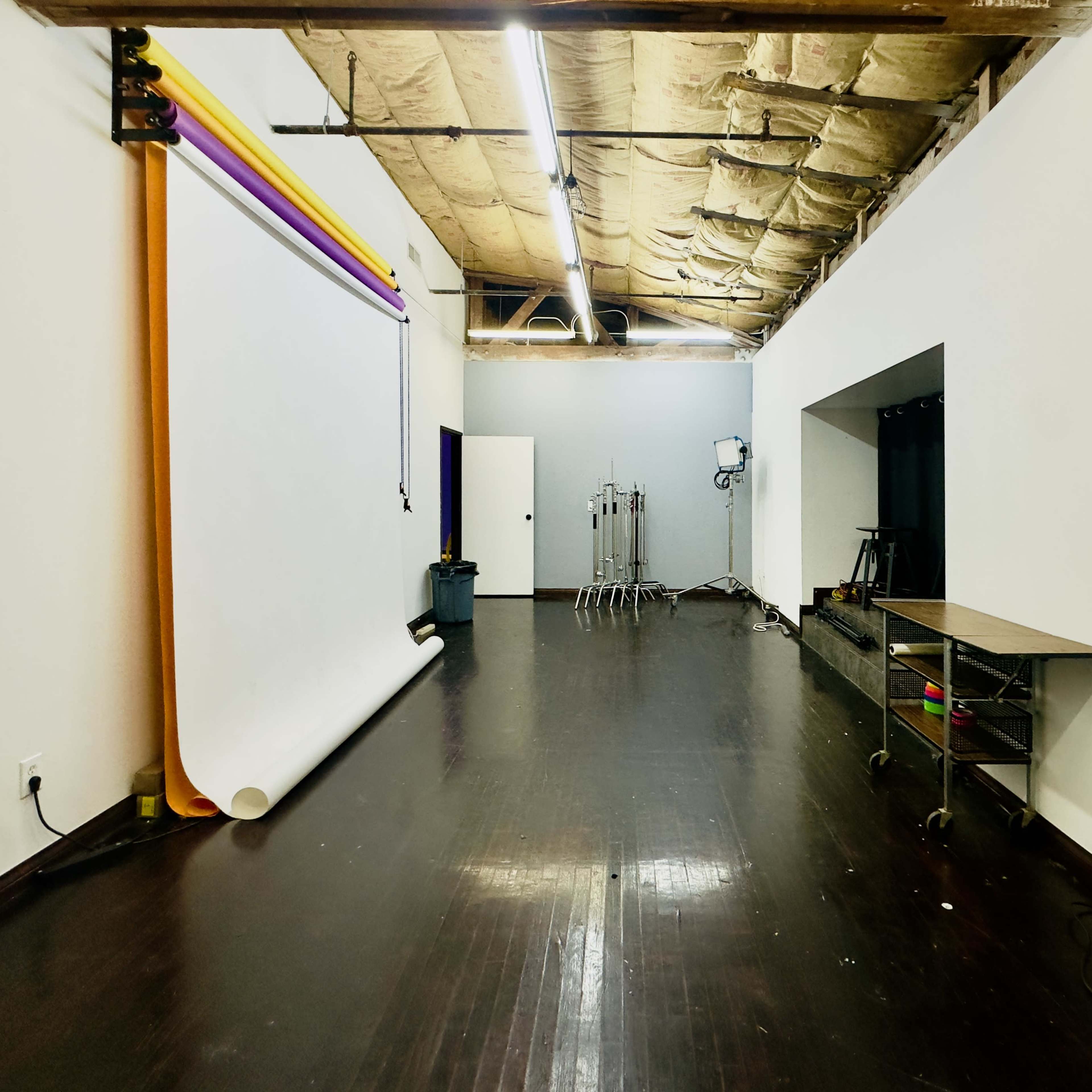 A spacious studio with a large seamless backdrop, a mirrorless wall, and various photography equipment set up along one side.