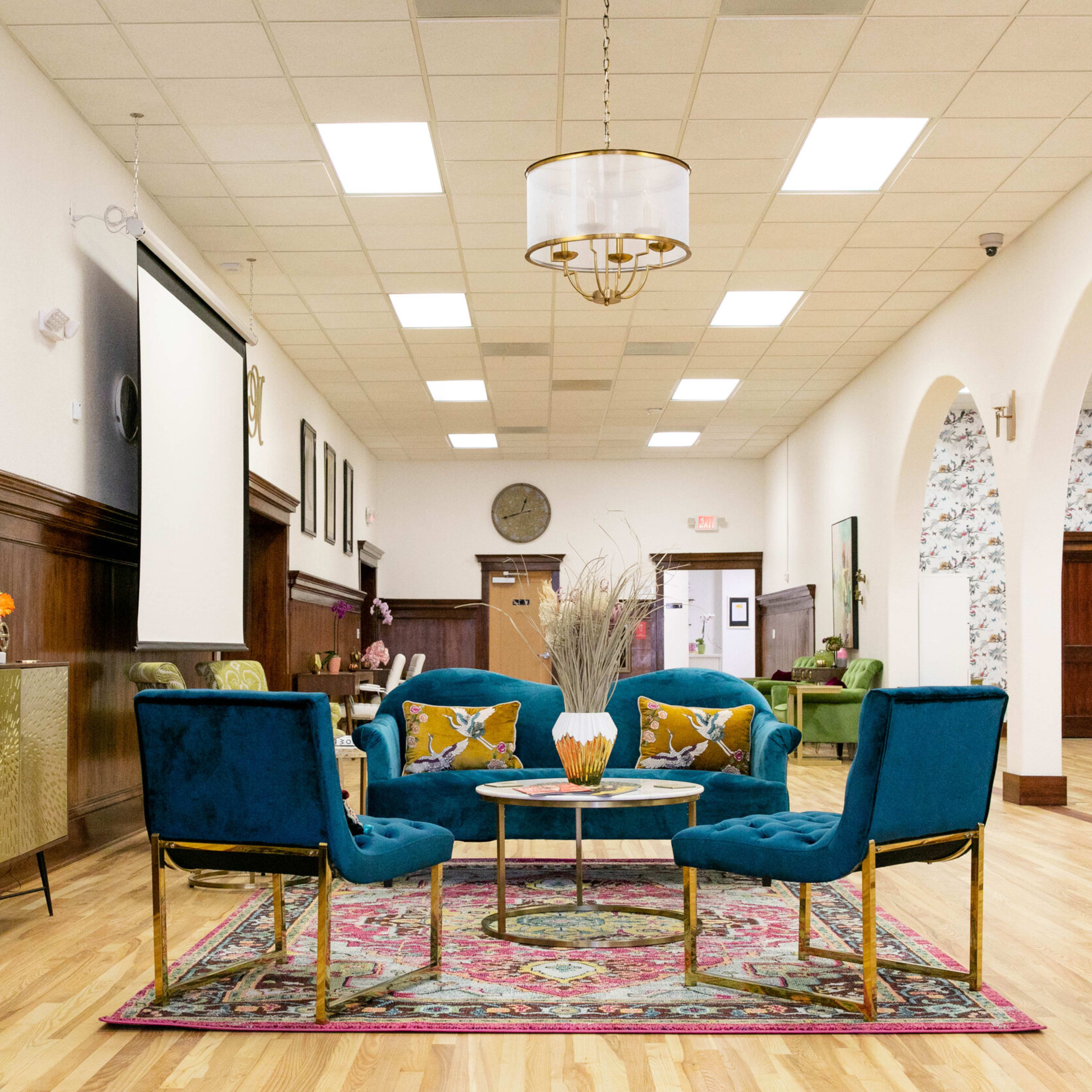 A spacious interior with wooden paneling, featuring a seating area with four blue chairs around a coffee table on a patterned rug, along with decorative furnishings and wall art.
