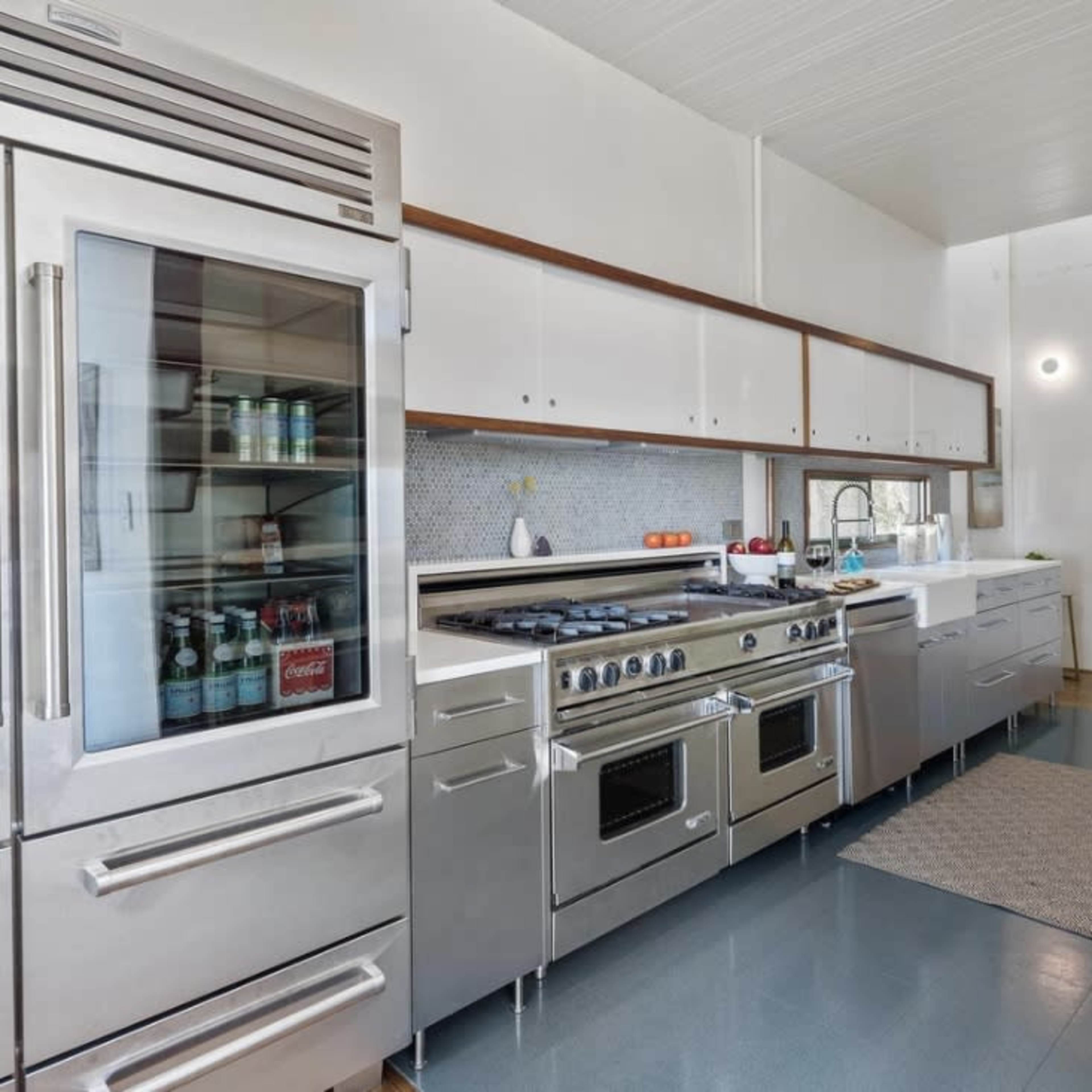 A modern kitchen featuring stainless steel appliances, a large refrigerator, and a cooking range, with white cabinetry and a blue floor.