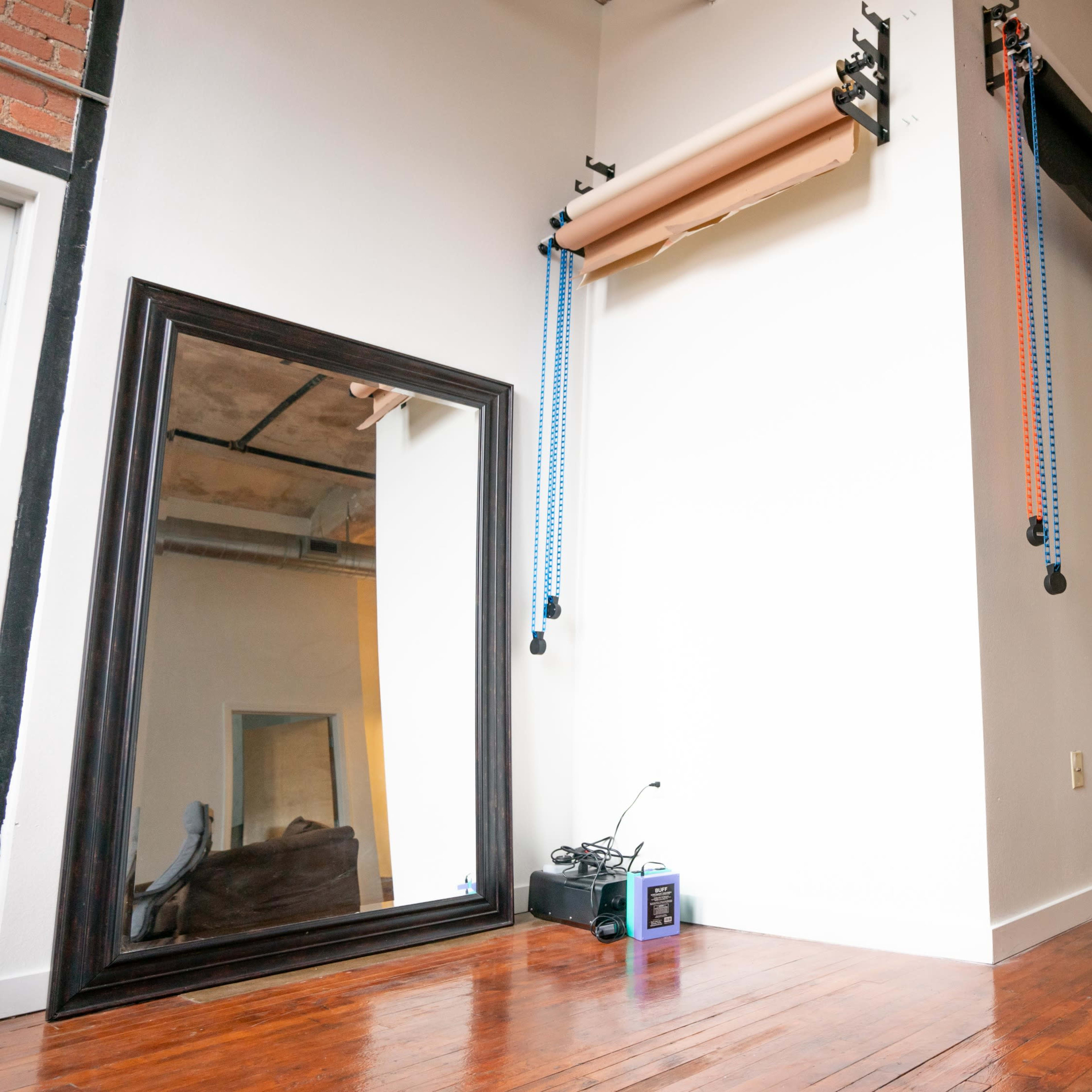 A studio space with a large mirror on one wall, backdrops mounted and hanging on the ceiling, and a circular reflector on the hardwood floor.