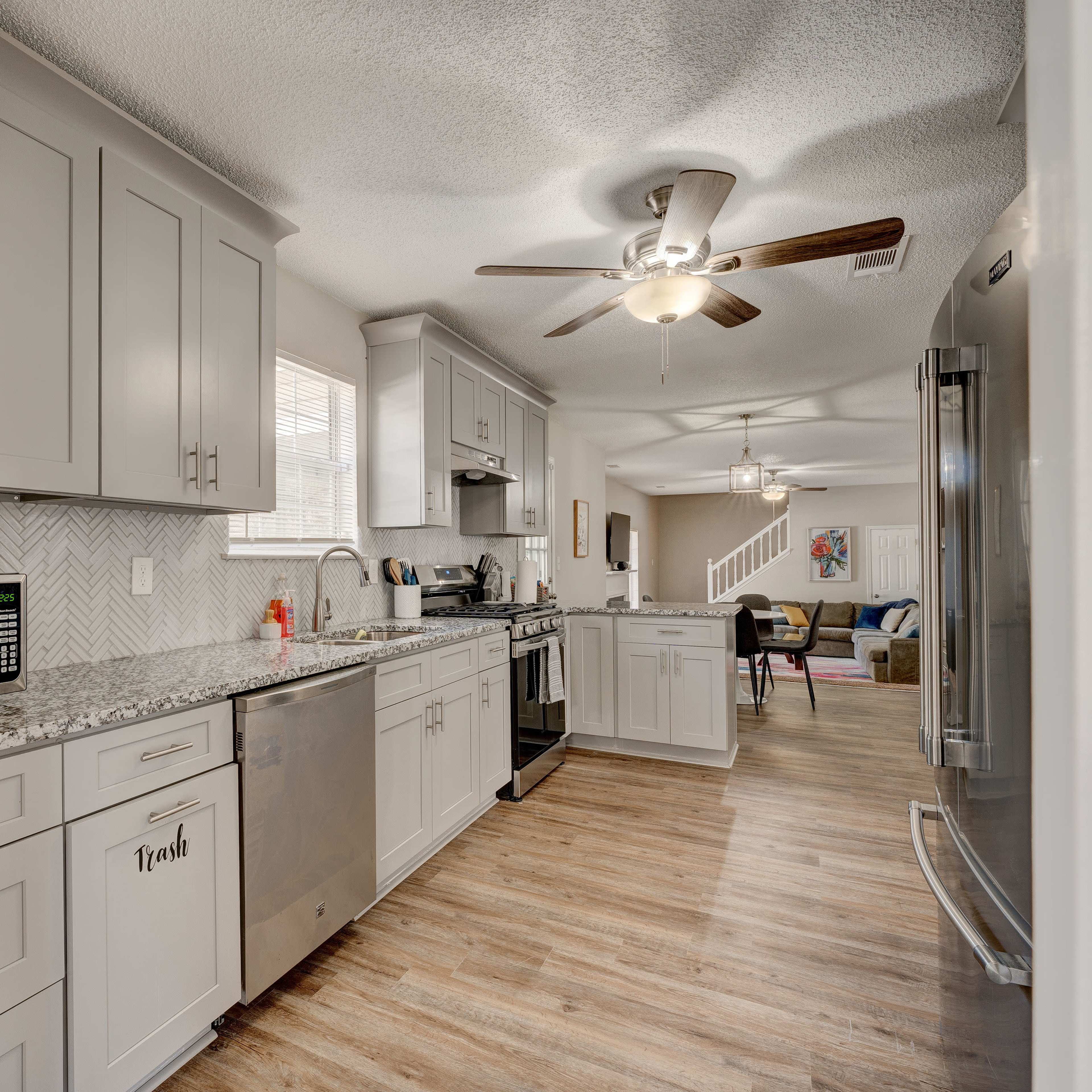 A modern kitchen features gray cabinets, stainless steel appliances, and a light-colored backsplash, with a dining area visible in the background.