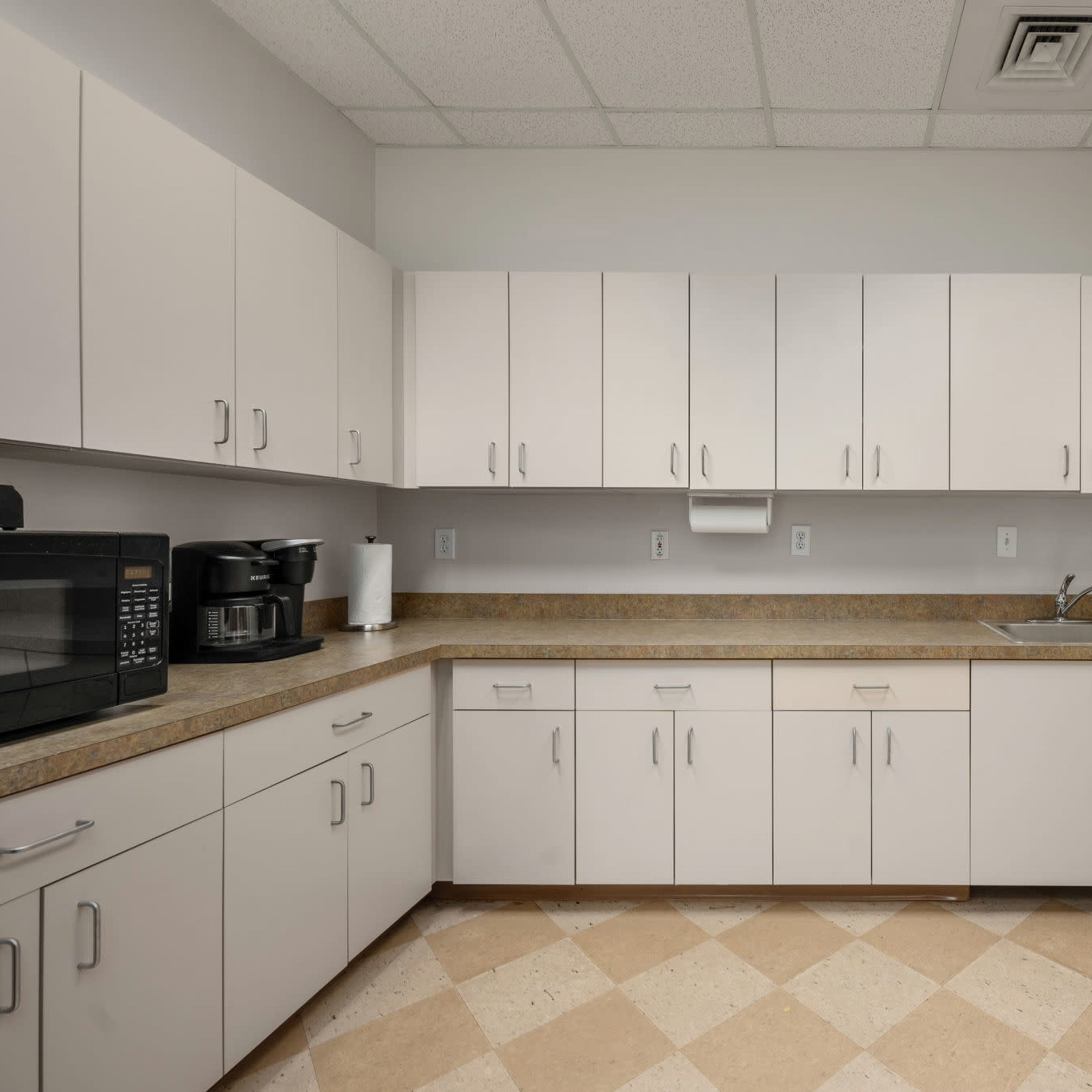 A clean, organized kitchen with light-colored cabinets and a countertop, featuring a microwave and a sink.