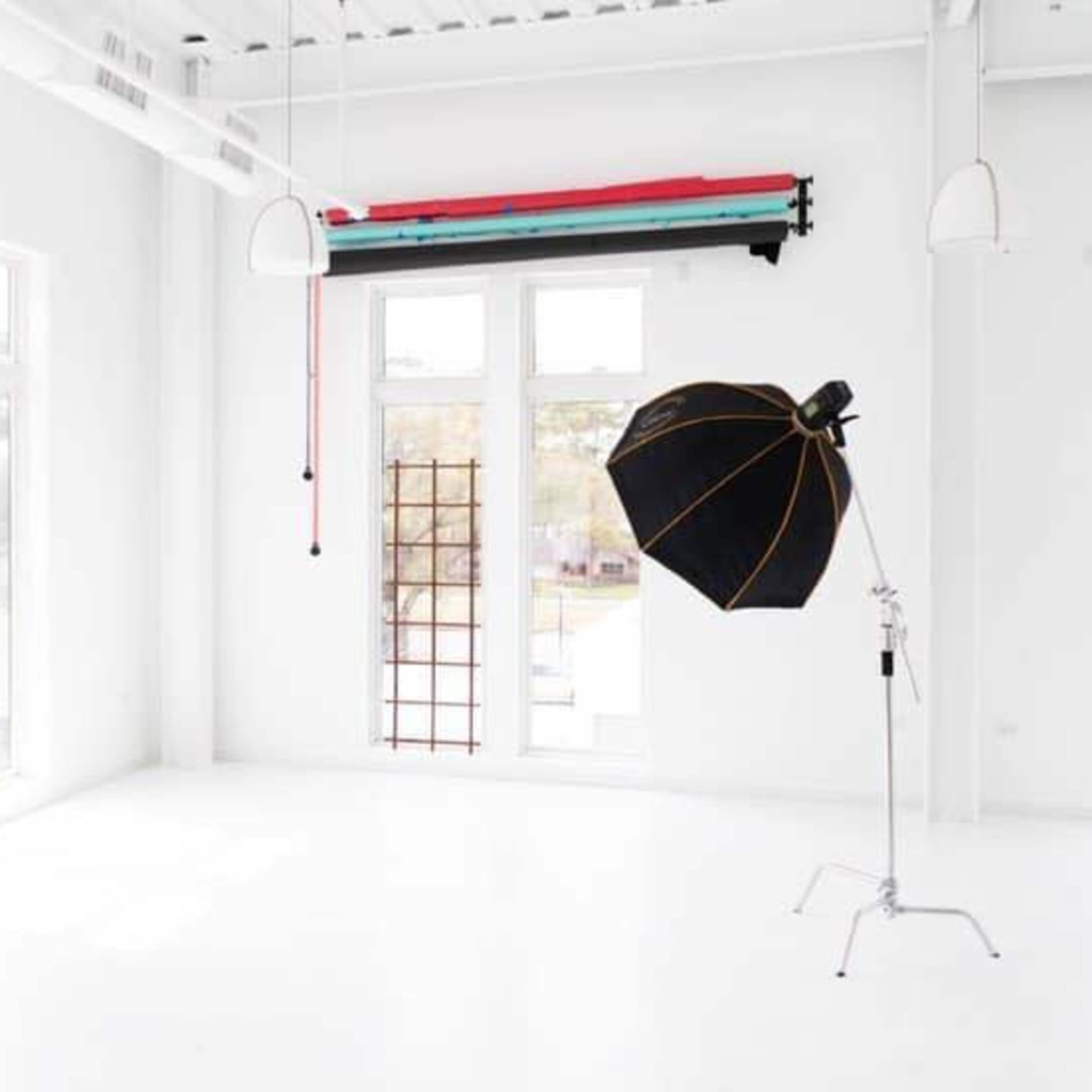 A bright, empty studio space with white walls, a large mirror, and a black photography umbrella on a silver stand.