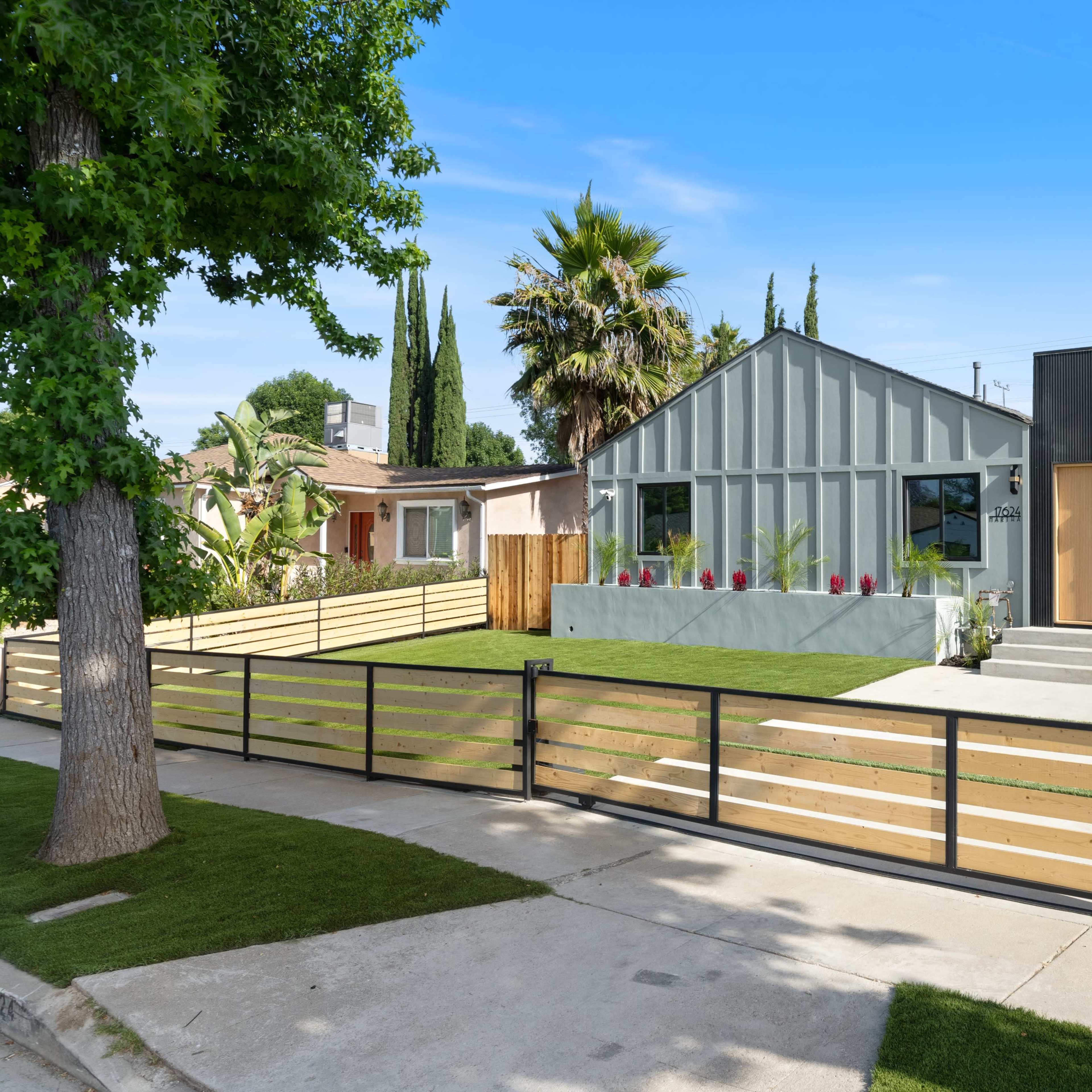 A modern duplex with a green lawn, two distinct house designs, and a wooden fence surrounding the property.