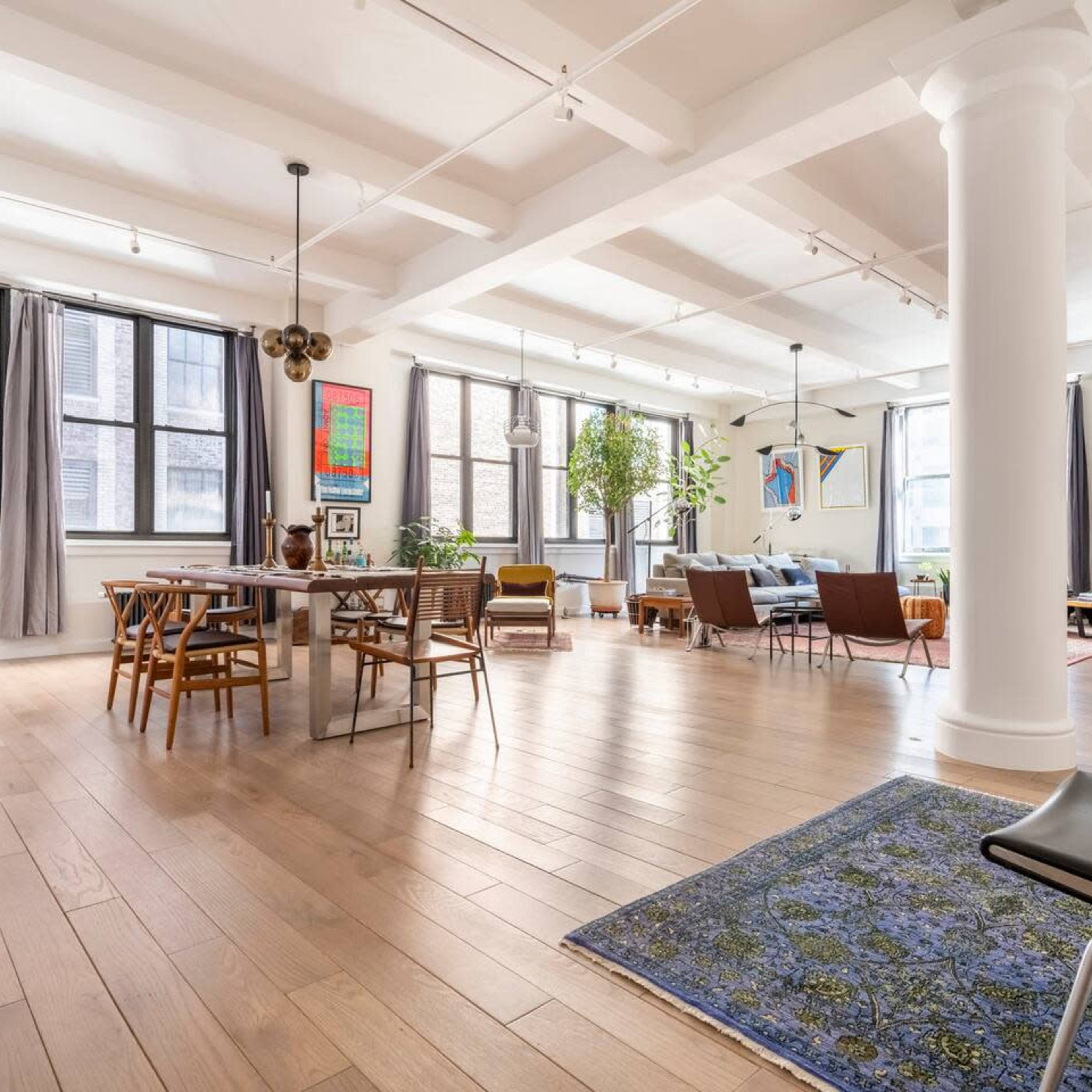 A spacious, modern interior with wooden floors, large windows, and a mix of dining and living areas furnished with various seats and decorative elements.