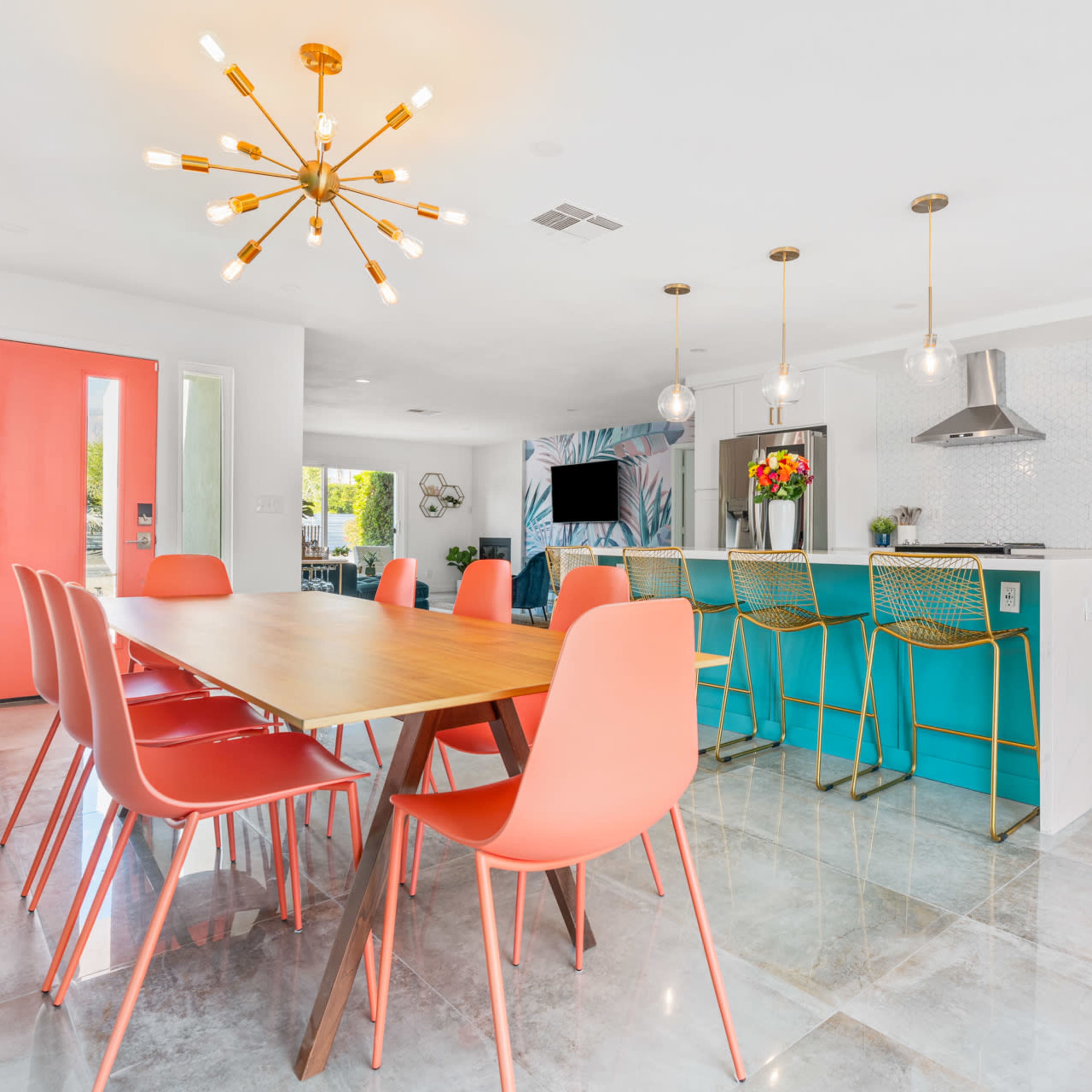 A modern kitchen and dining area with a wooden table surrounded by coral-colored chairs and a turquoise kitchen island.