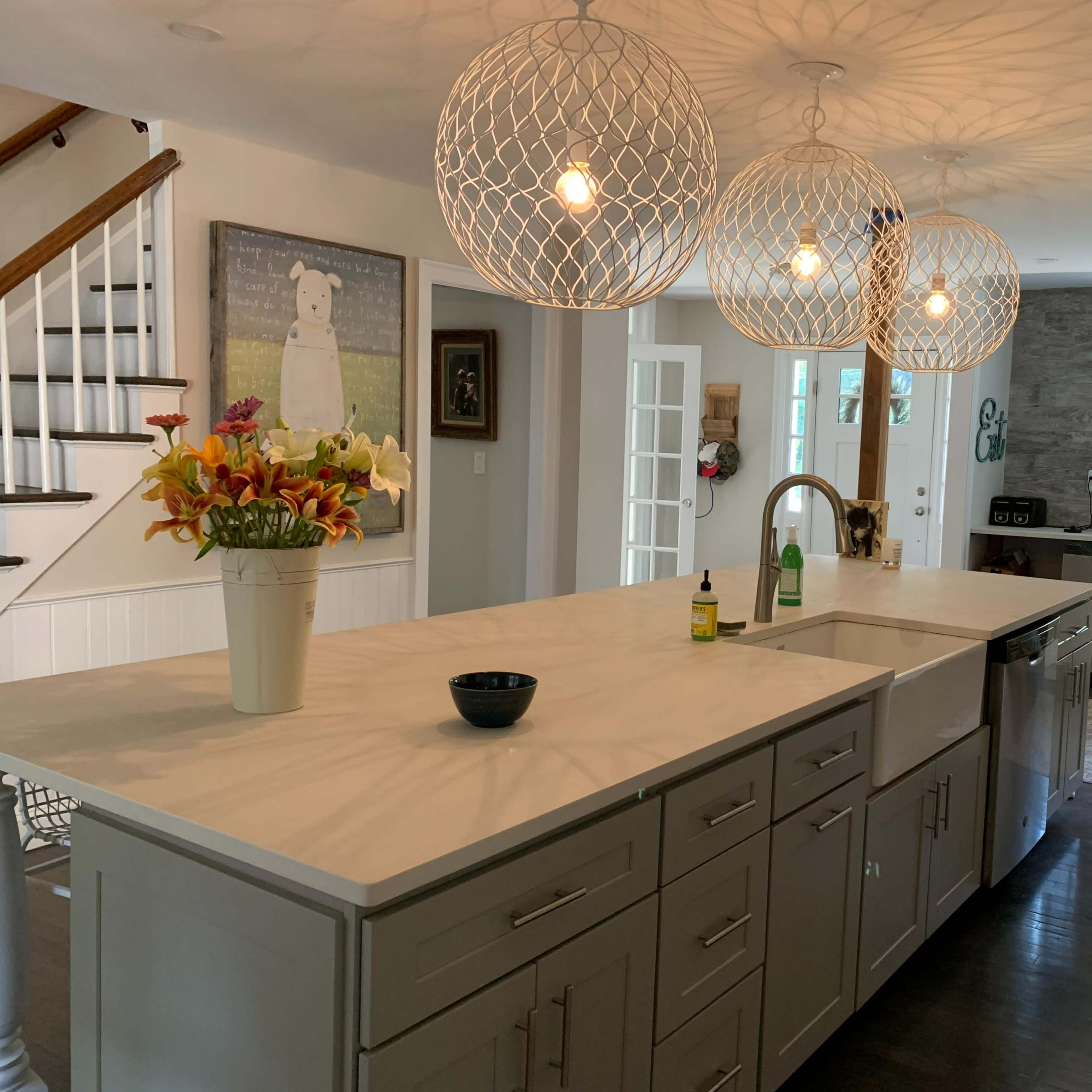 A modern kitchen featuring a large island with a marble countertop, three pendant lights overhead, and a vase of flowers on the island.