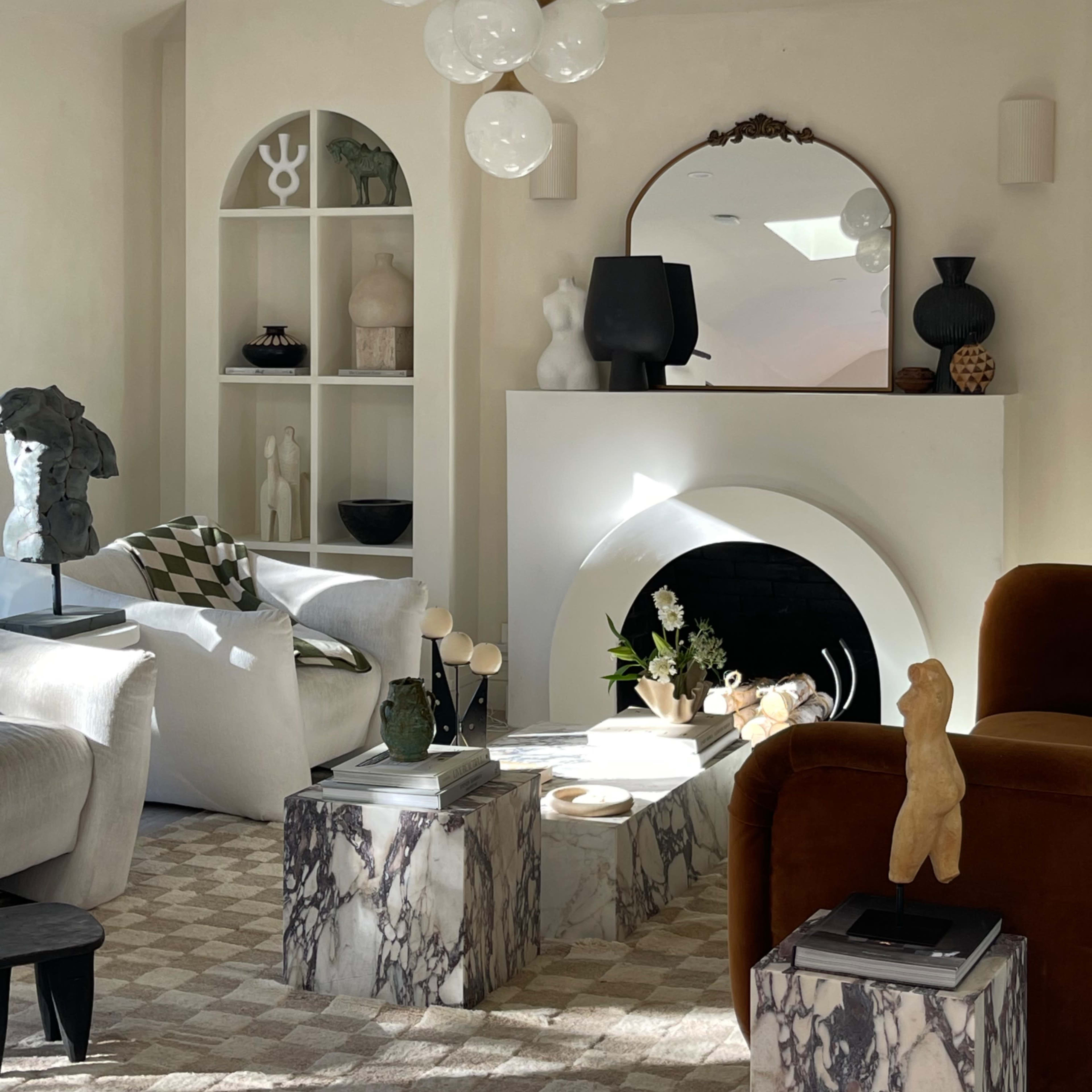 A modern living room featuring a stylish arrangement of furniture, art pieces, and decorative objects around a central fireplace.