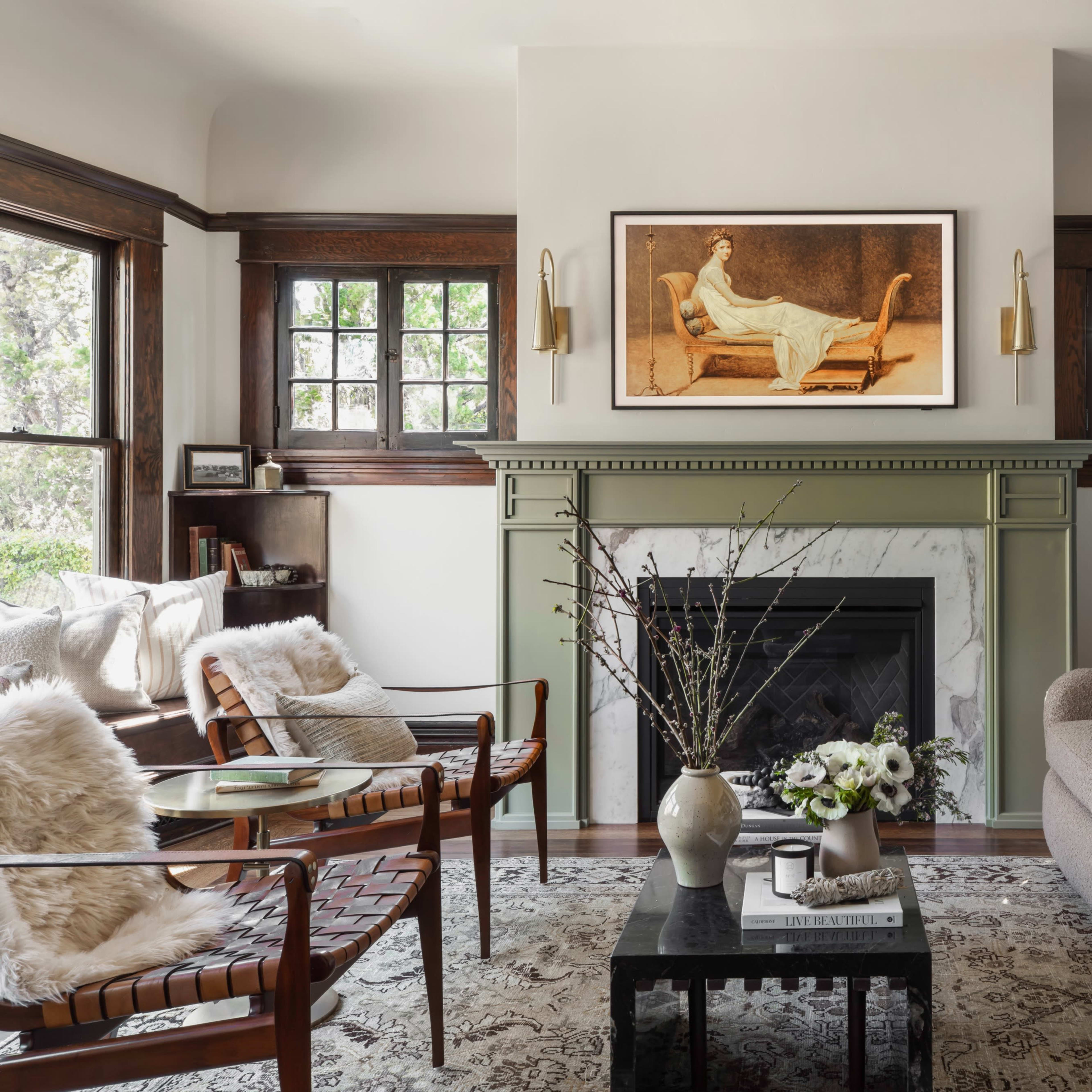 A cozy living room features a green fireplace, a beige sofa, and wooden chairs with large windows letting in natural light.