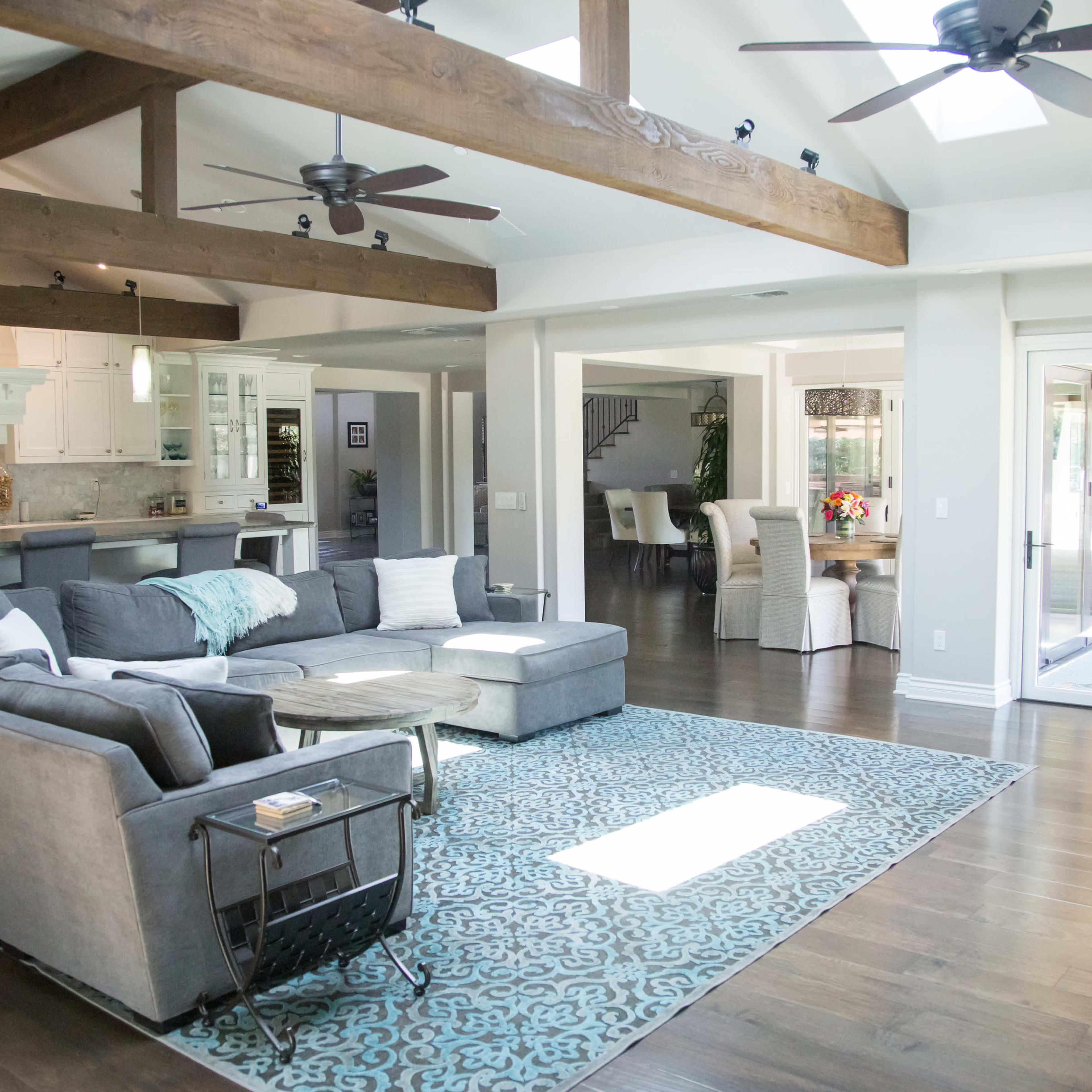 A spacious living room featuring a large sectional sofa, wooden beams on the ceiling, and sliding glass doors leading to an outdoor area.