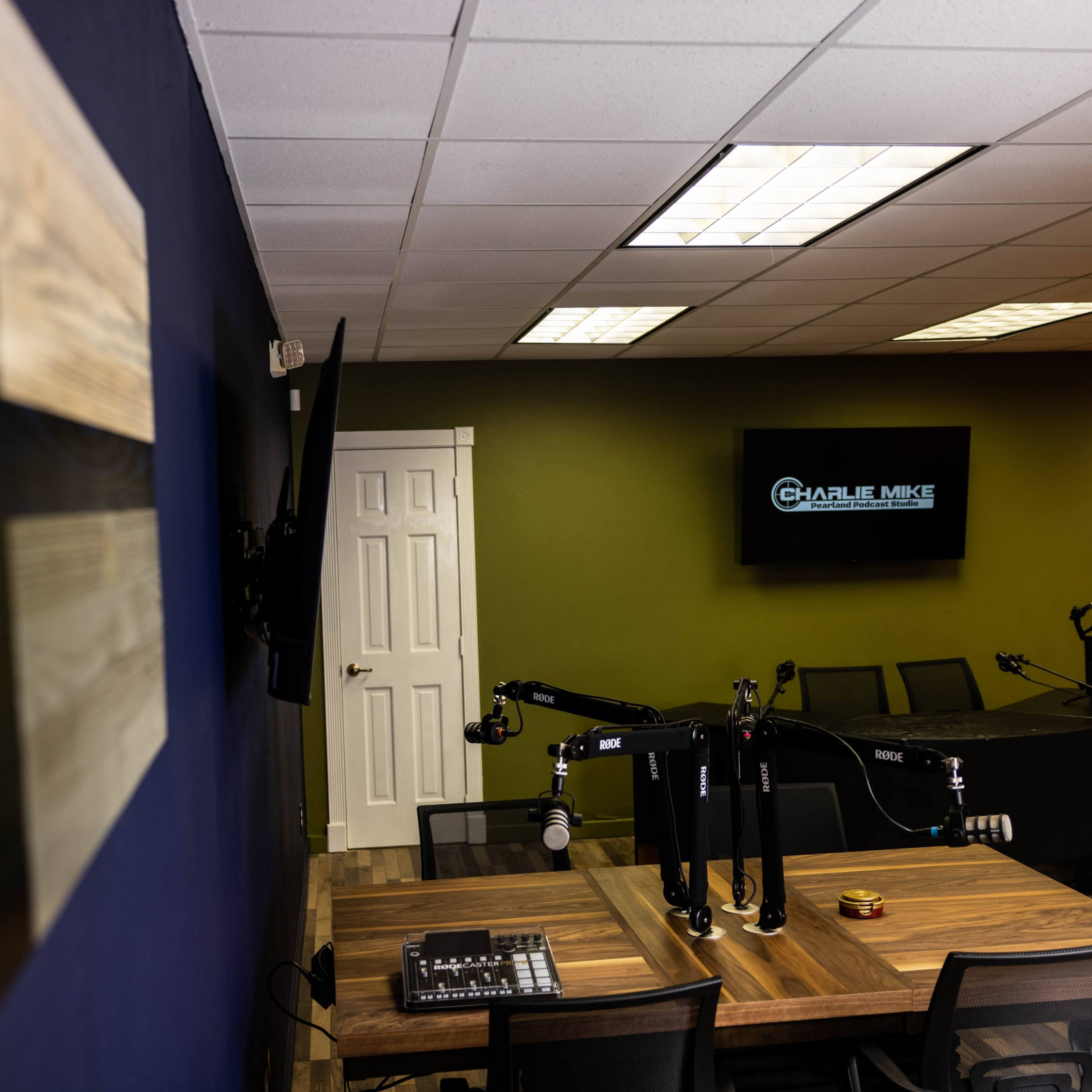 A podcast studio featuring a large table with microphones, a television display, and a Texas flag on the wall.