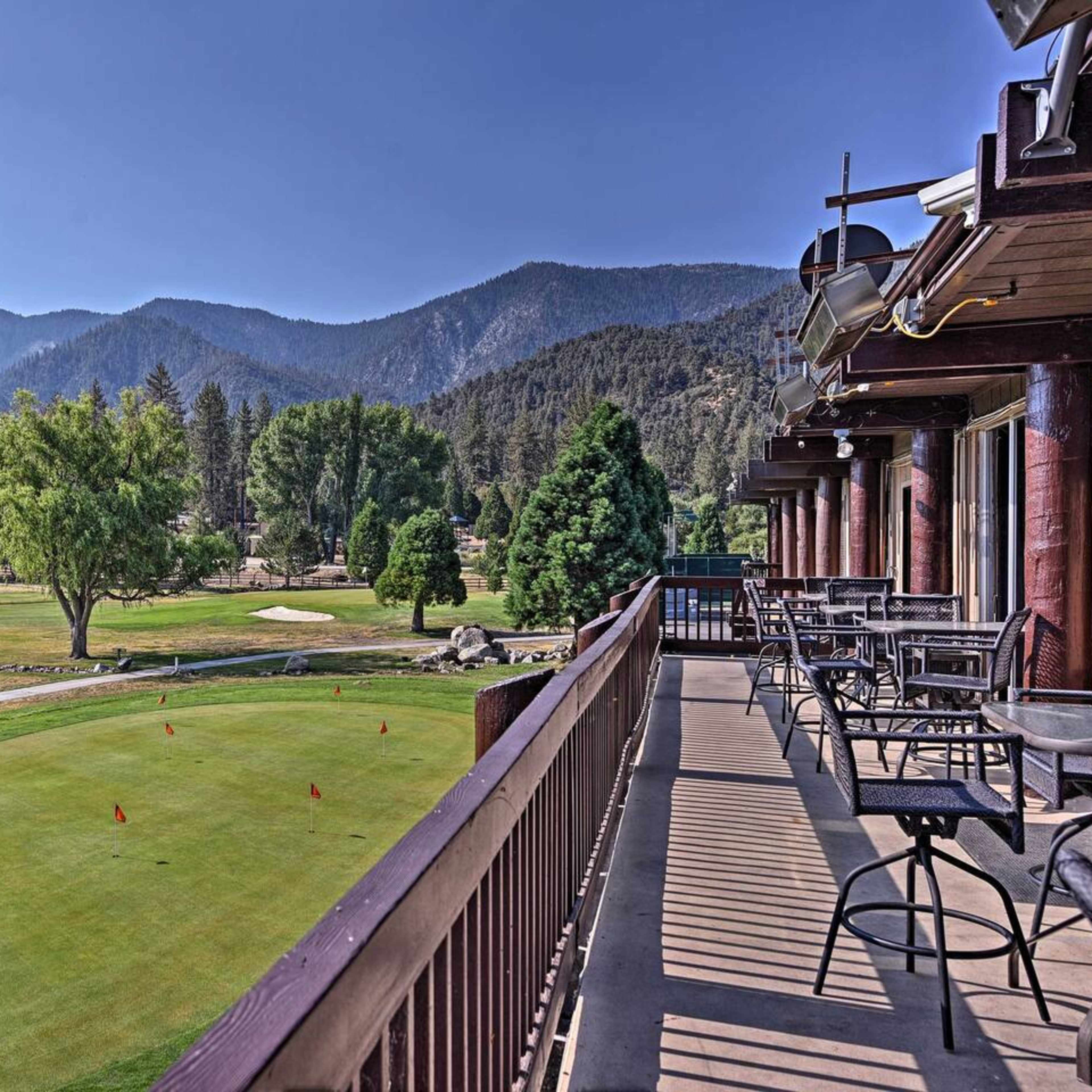 A balcony overlooks a golf course with a putting green, trees, and mountains in the background.