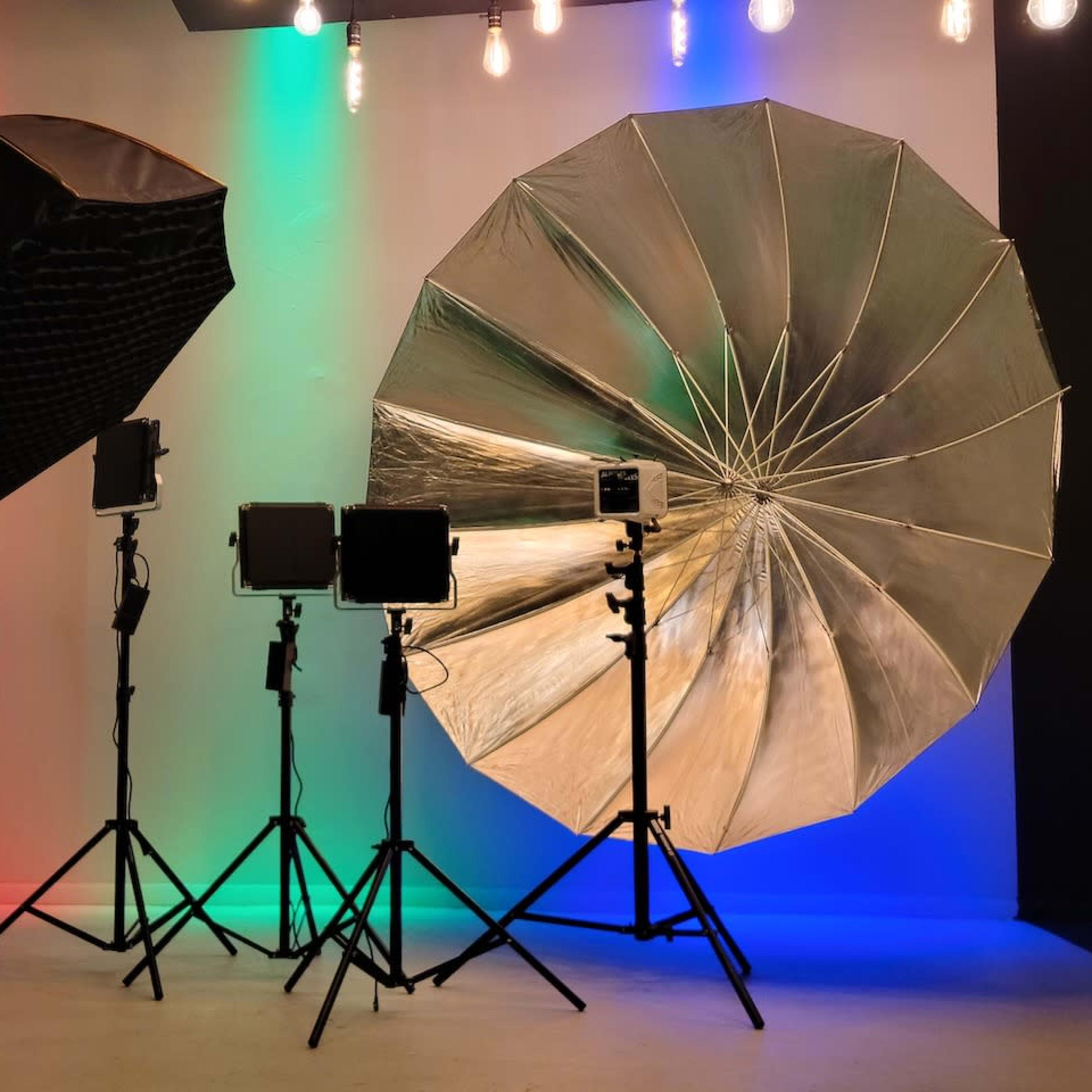 Studio lighting equipment, including softbox and umbrella lights, set up against a backdrop with colored lighting.