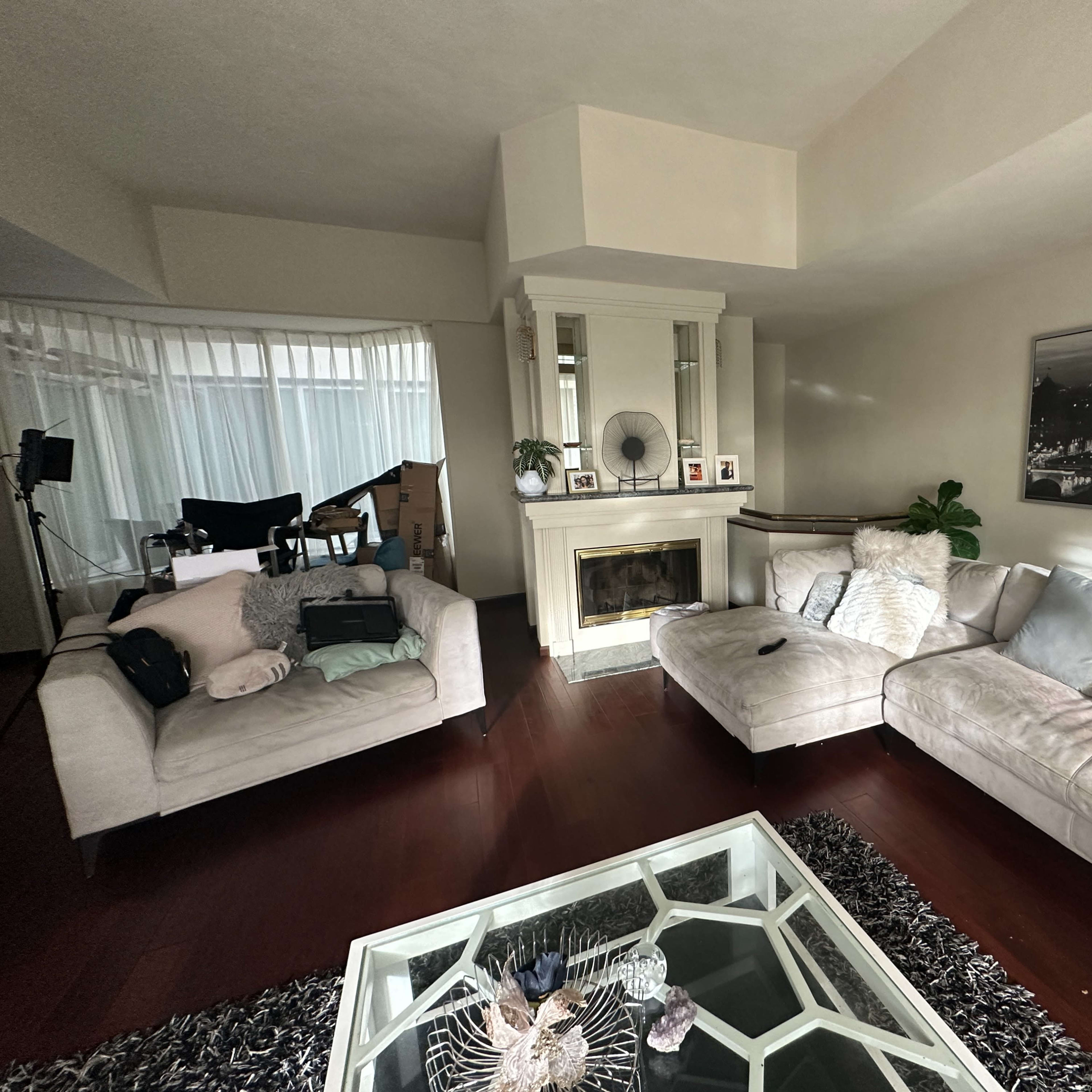 A spacious living room with two light-colored sofas, a glass coffee table, and a fireplace surrounded by decorative items.