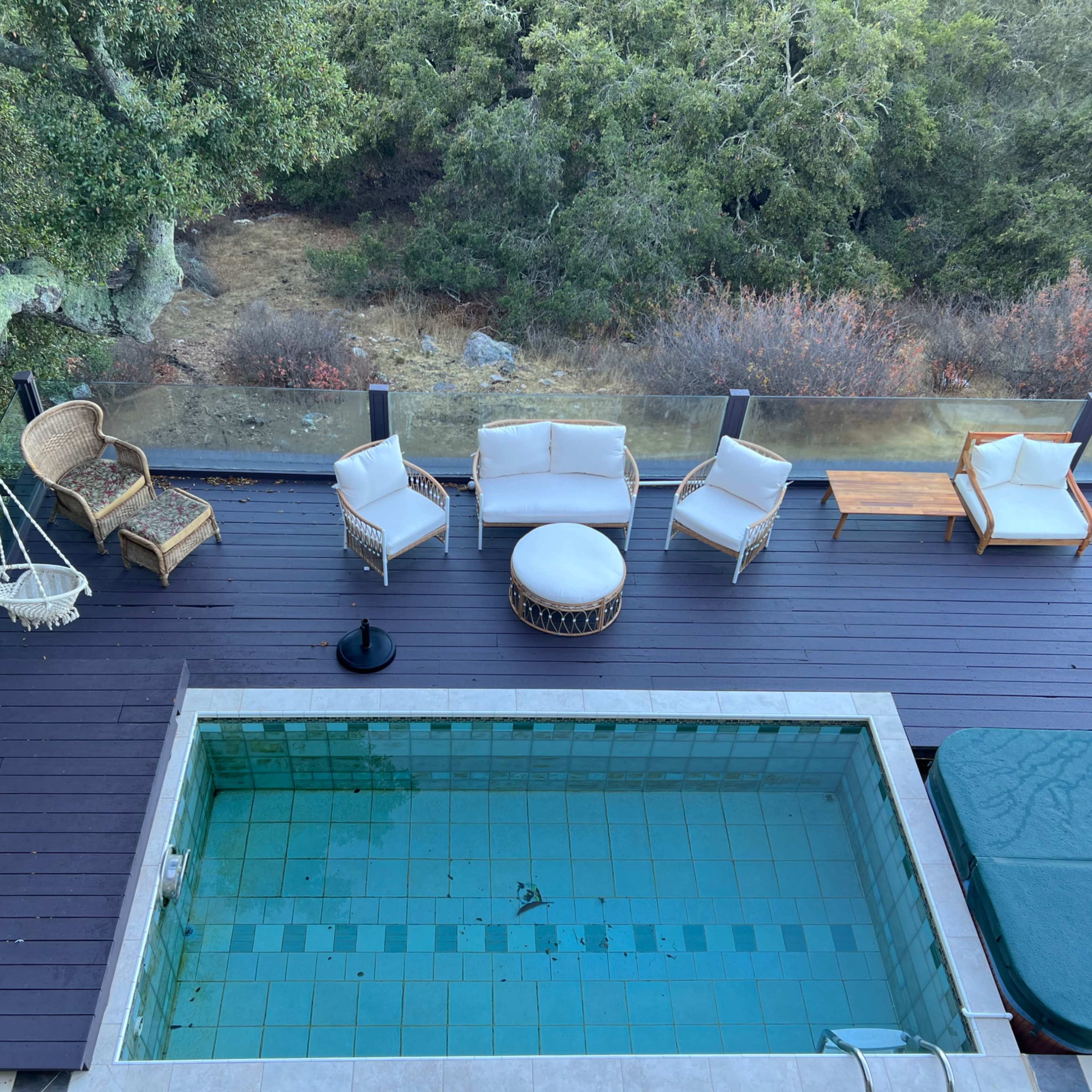 A balcony with a small pool and several pieces of outdoor furniture, including chairs and a round table, surrounded by greenery.