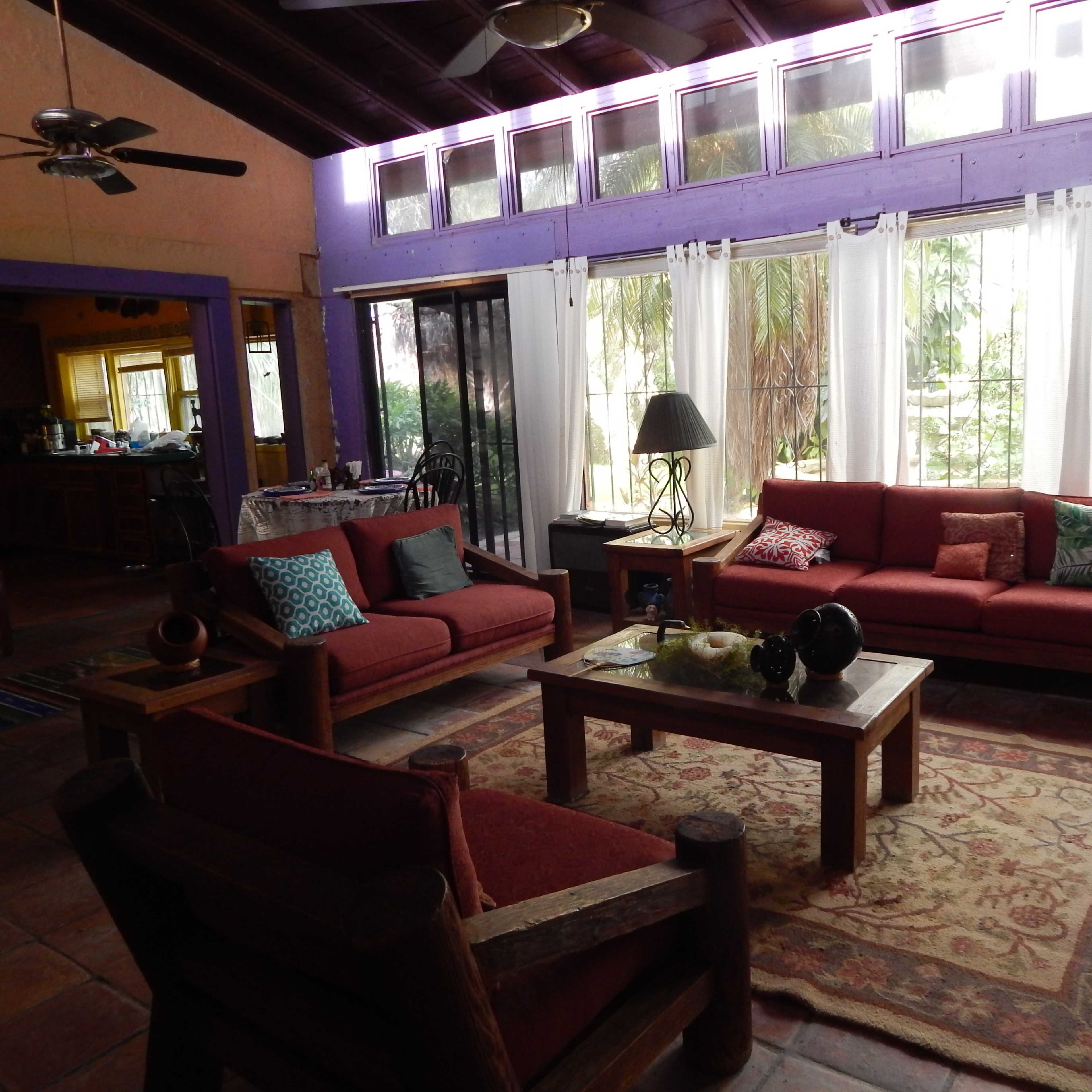 A living room with two red sofas, a wooden coffee table, and large windows allowing natural light to illuminate the space.
