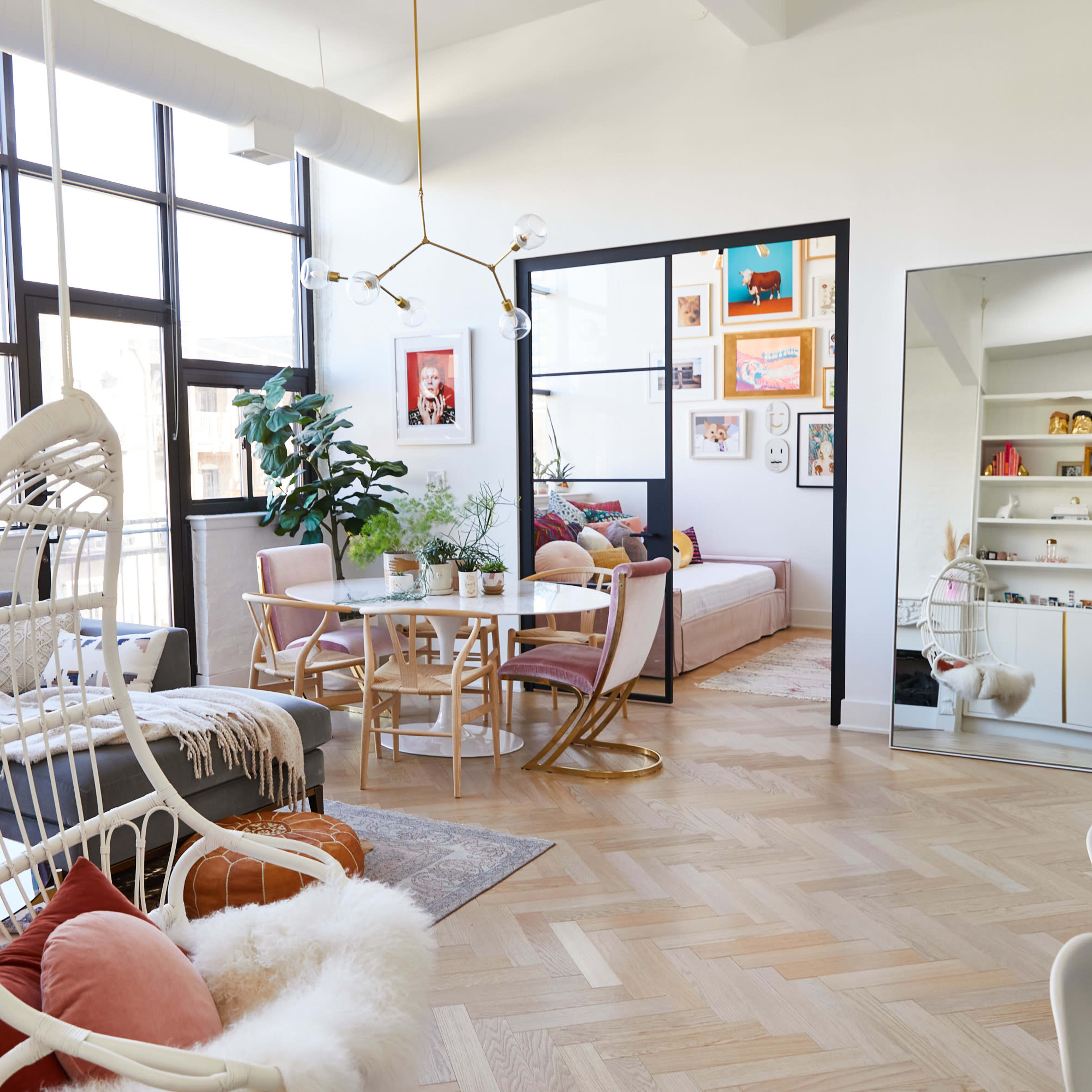 A stylish living area with a seating arrangement, a dining table, and large windows, featuring modern decor and plants.