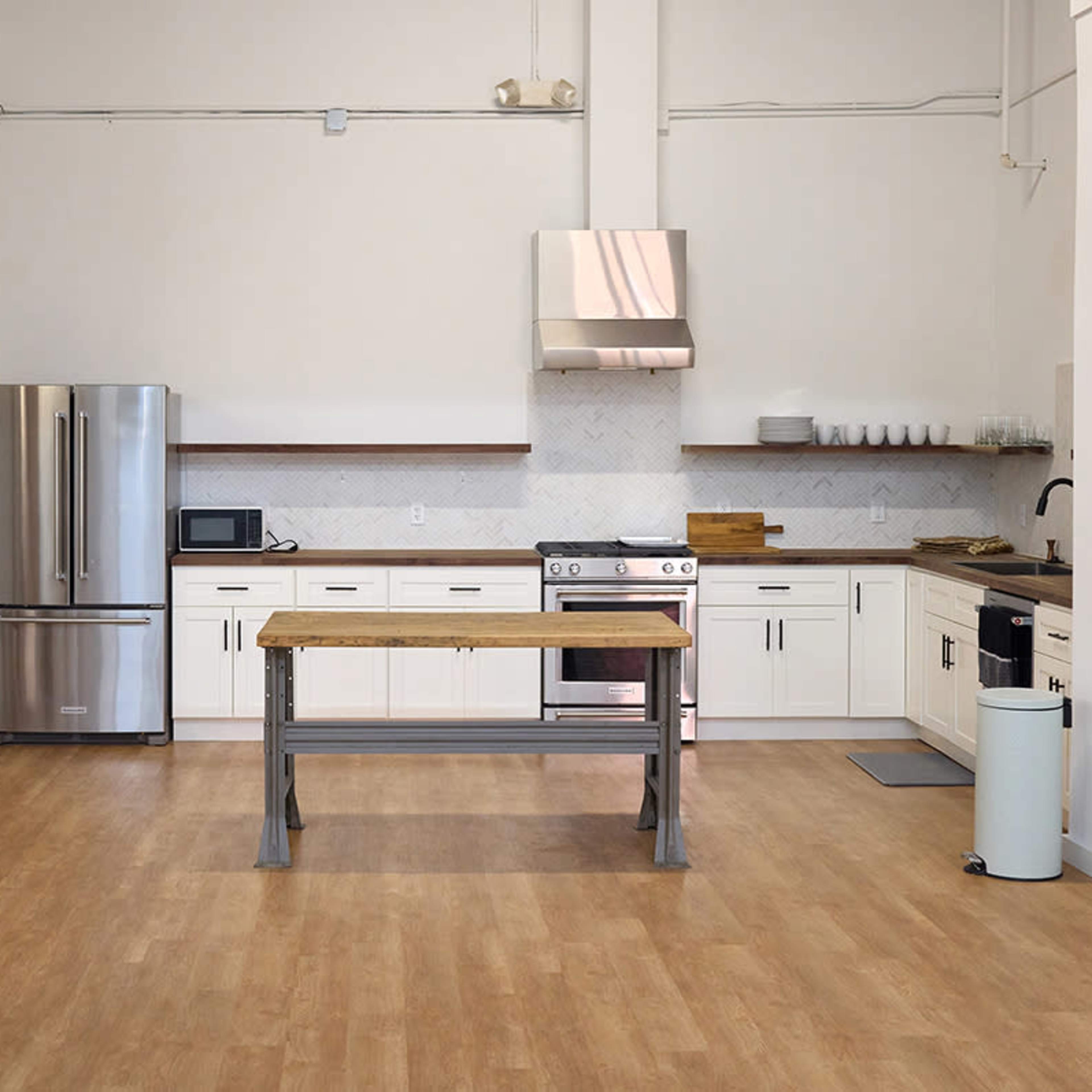 A modern kitchen with white cabinets, stainless steel appliances, a wooden island table, and large glass sliding doors.