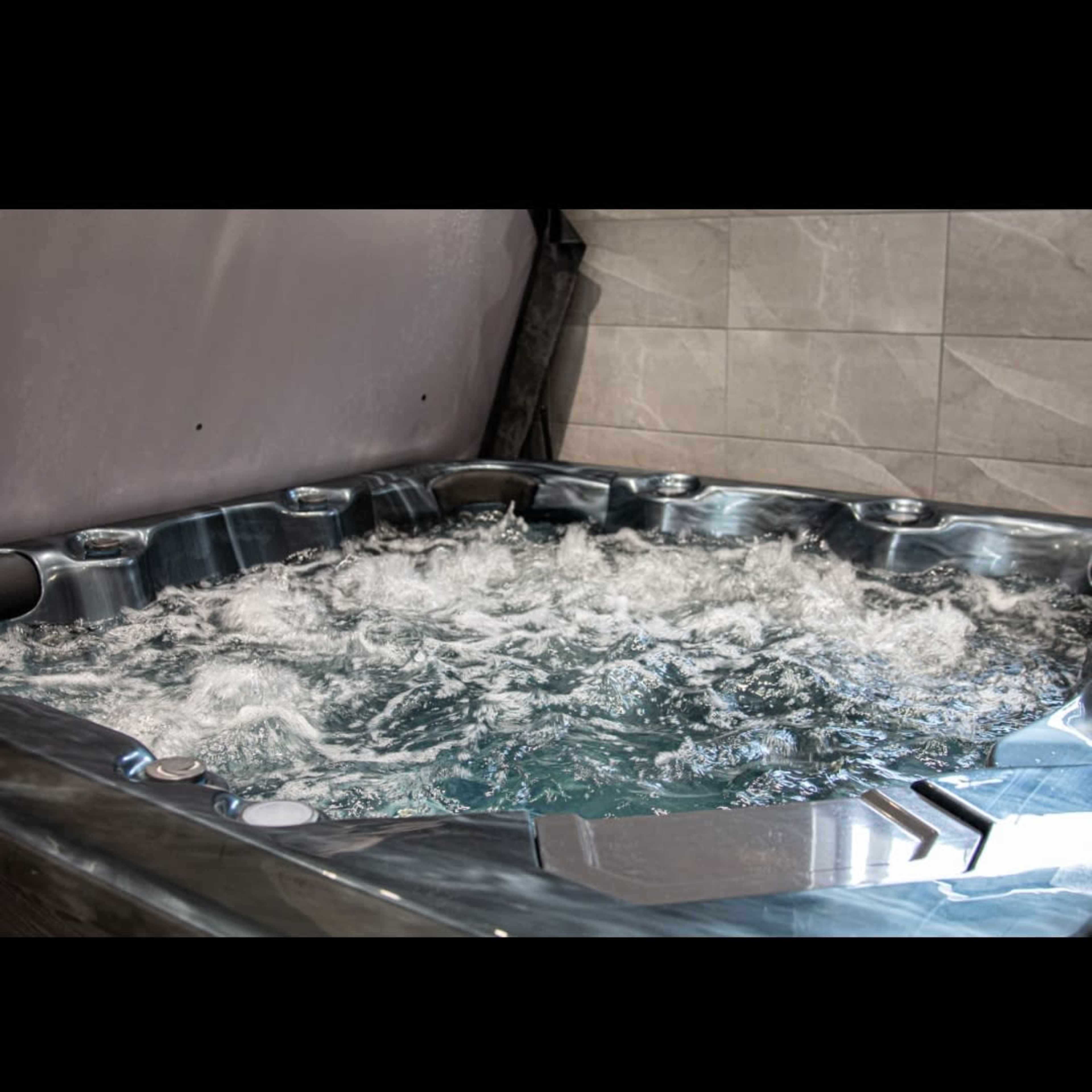 A hot tub with bubbling water is positioned against a tiled wall.