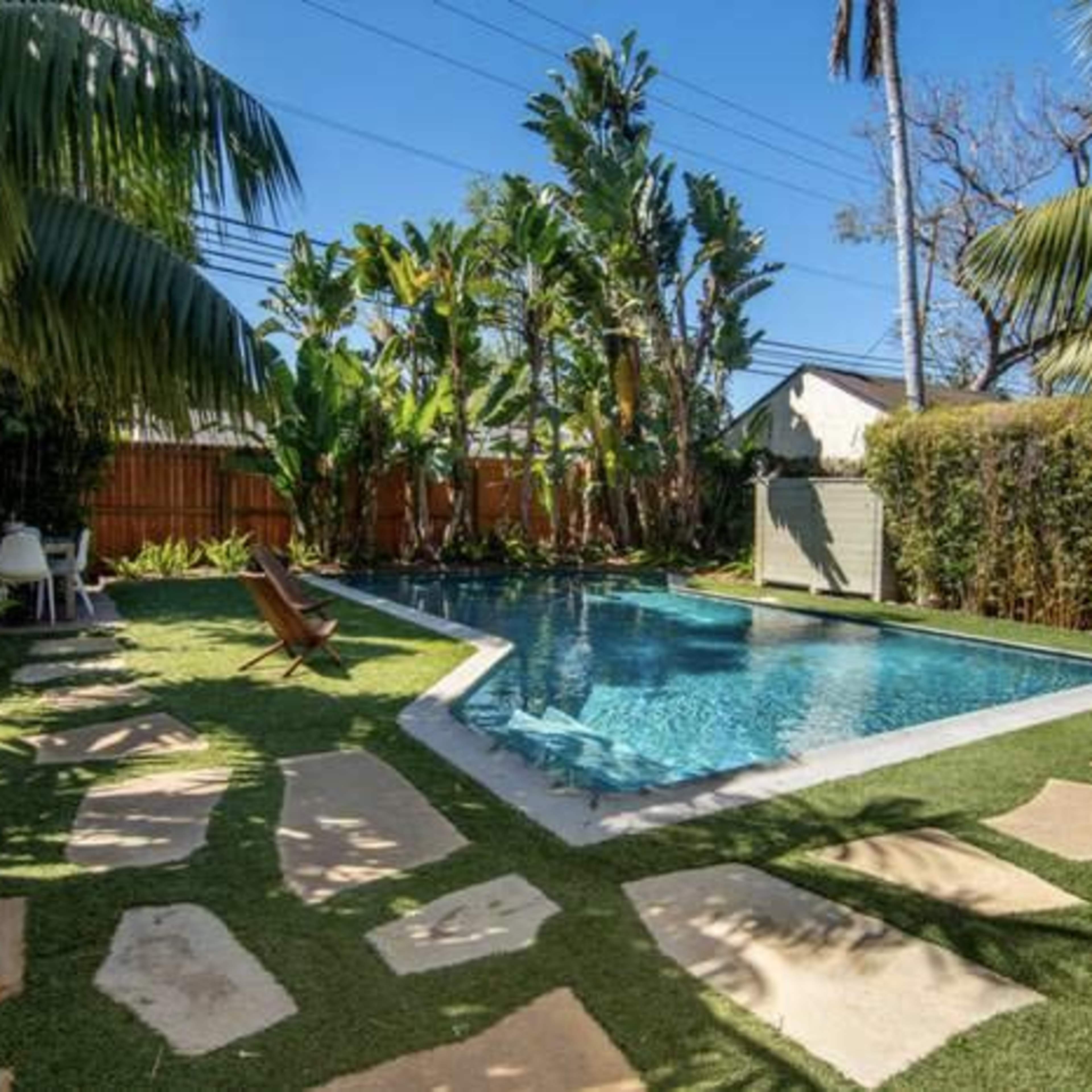A backyard with a swimming pool surrounded by tropical plants and stone pathways.