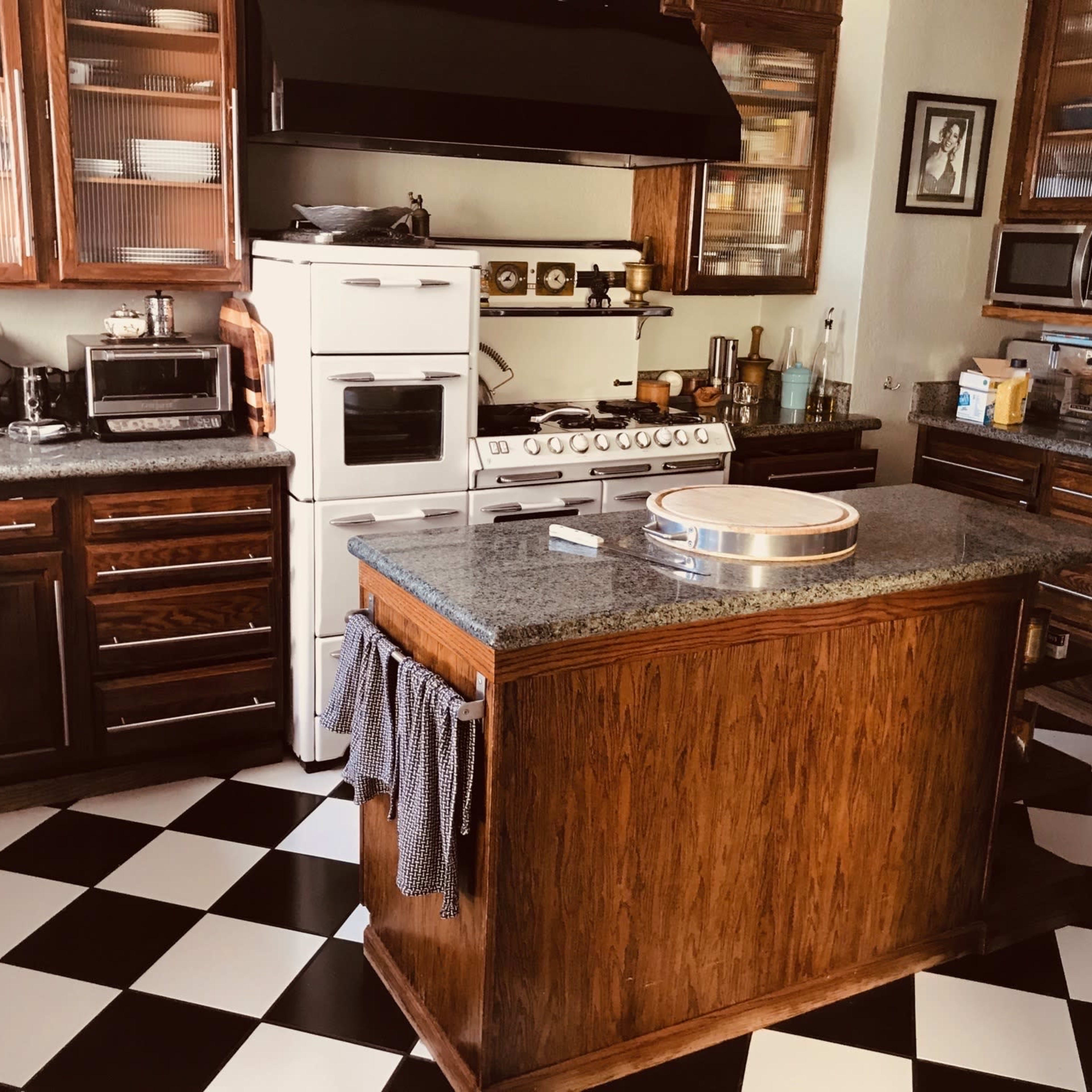 The kitchen features dark wooden cabinets, a central island with a round cutting board, and black-and-white checkered flooring.
