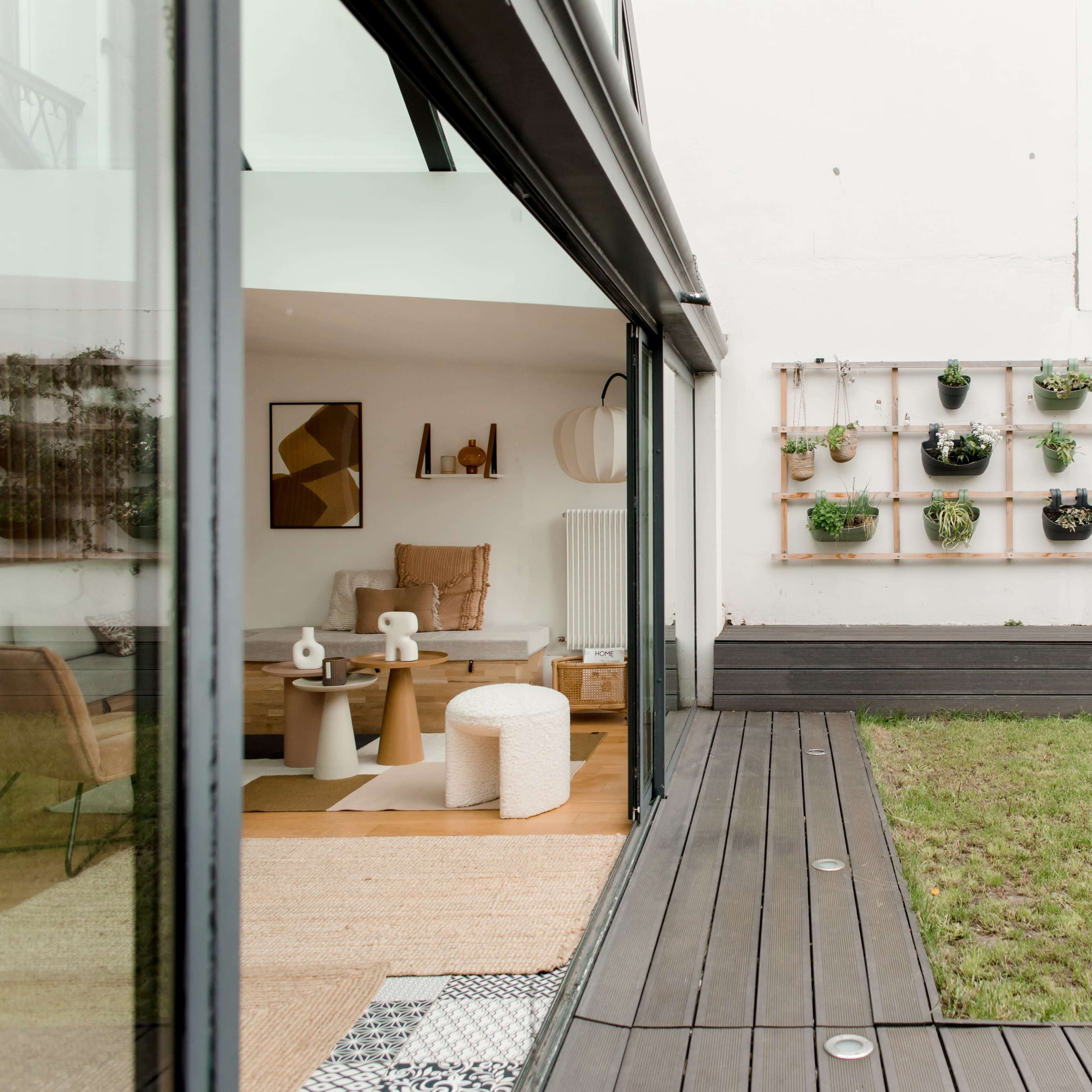 A modern outdoor space features a grassy area, wooden decking, and a wall-mounted garden with various plants.