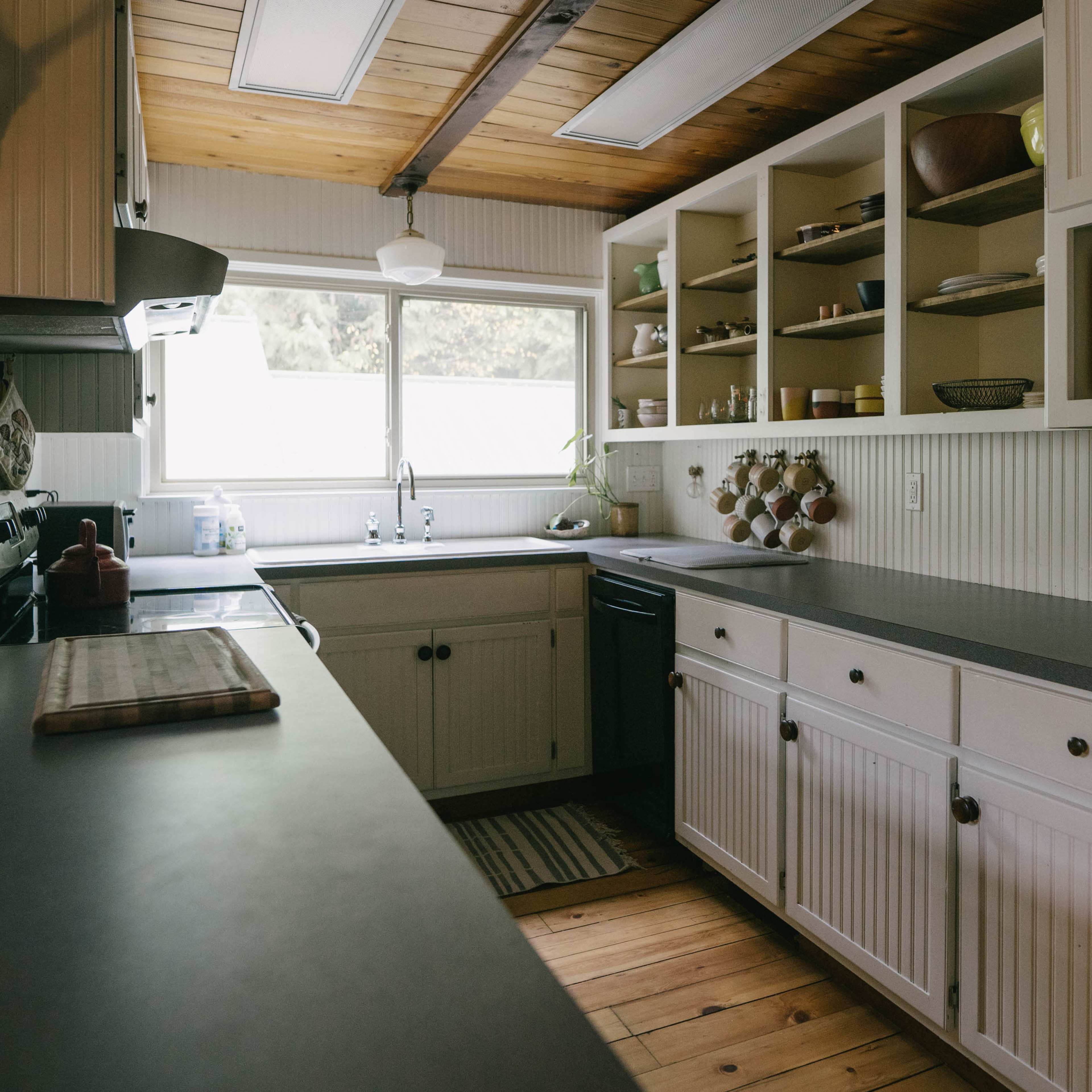 The kitchen features white cabinetry, a black countertop, and open shelving displaying various kitchen items, with a window providing natural light.