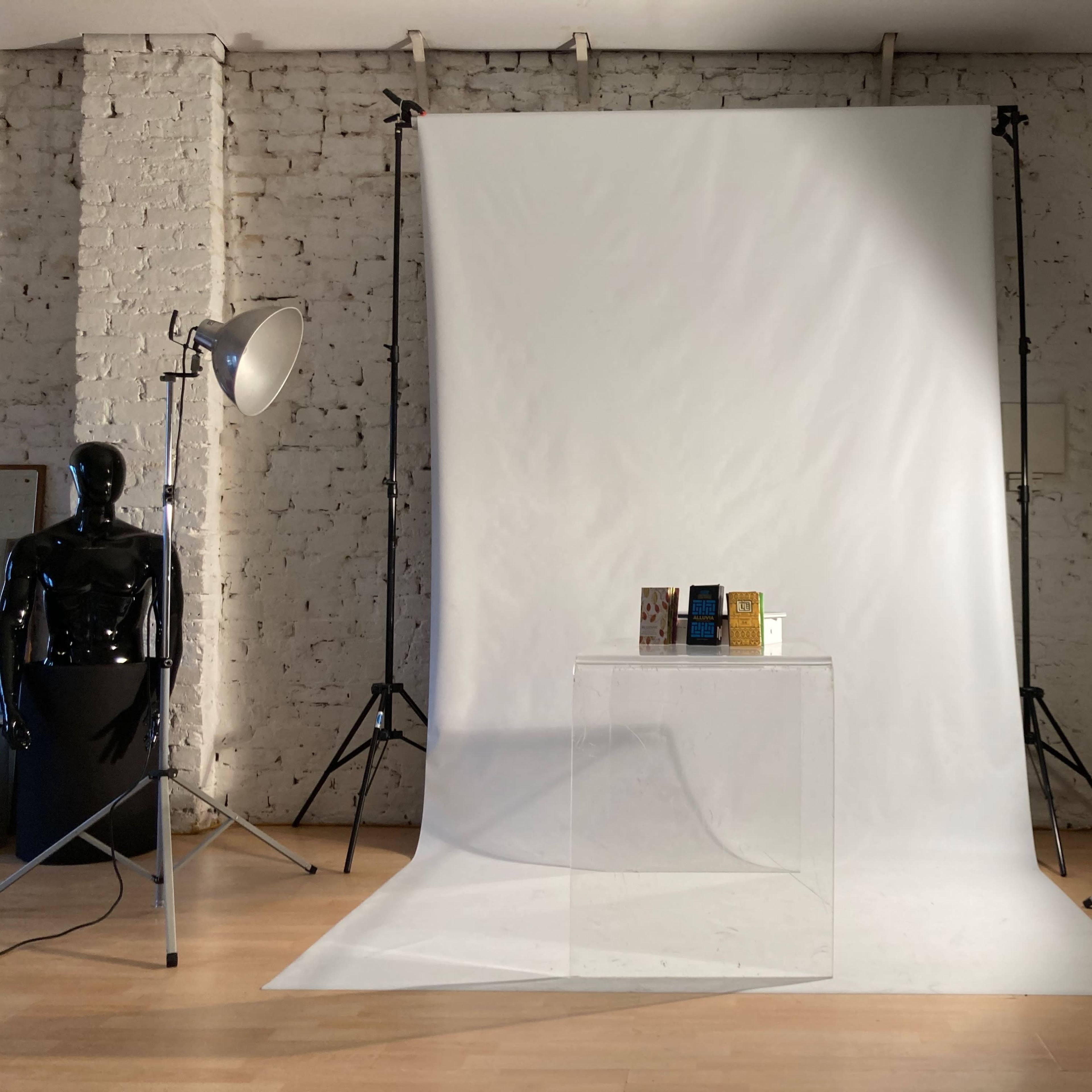 A minimalist studio setup with a clear display table centered in front of a white backdrop, flanked by two lighting equipment stands.