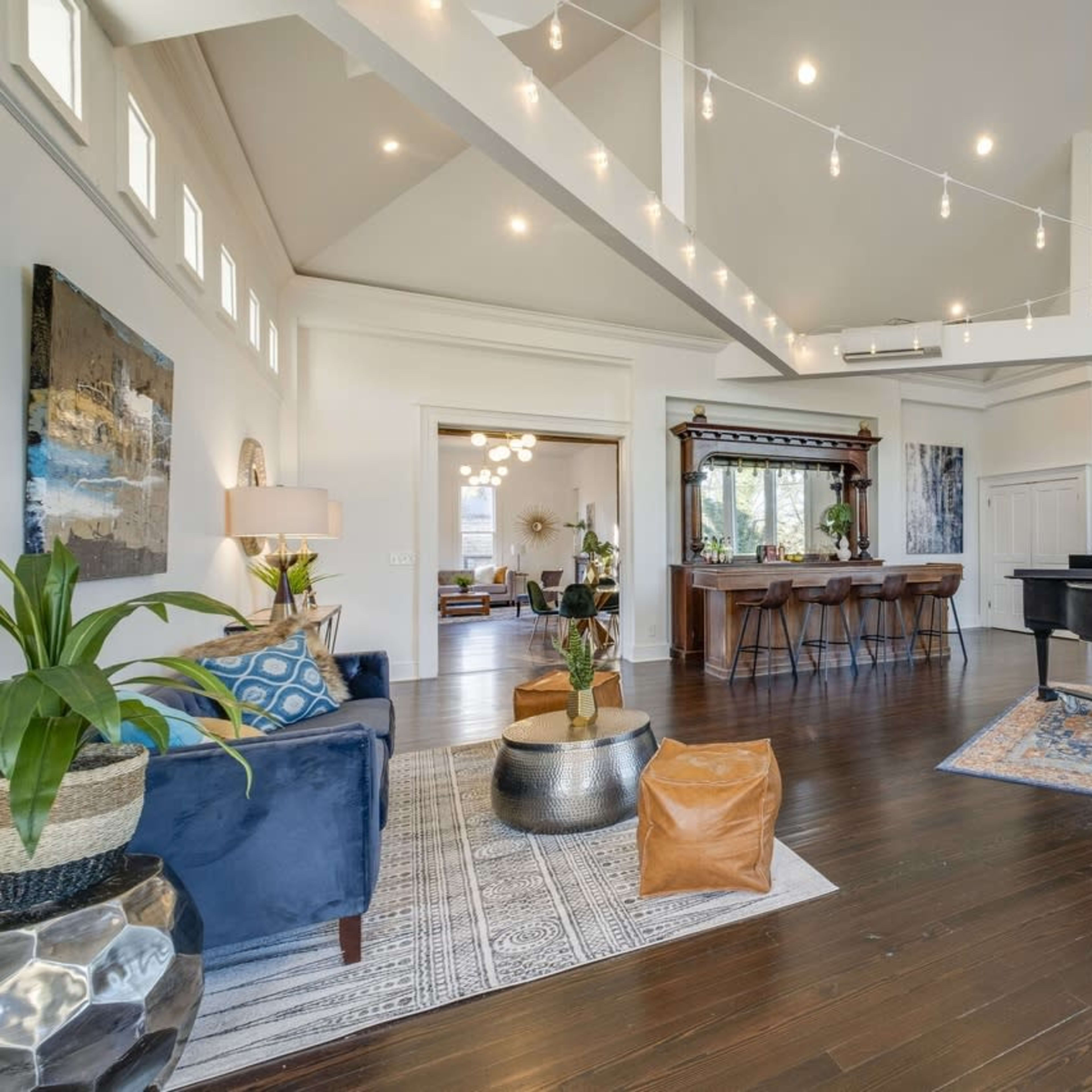 A spacious, well-lit living area features a grand piano, modern furnishings, and artistic decorations, with an open view to a bar area and additional seating.