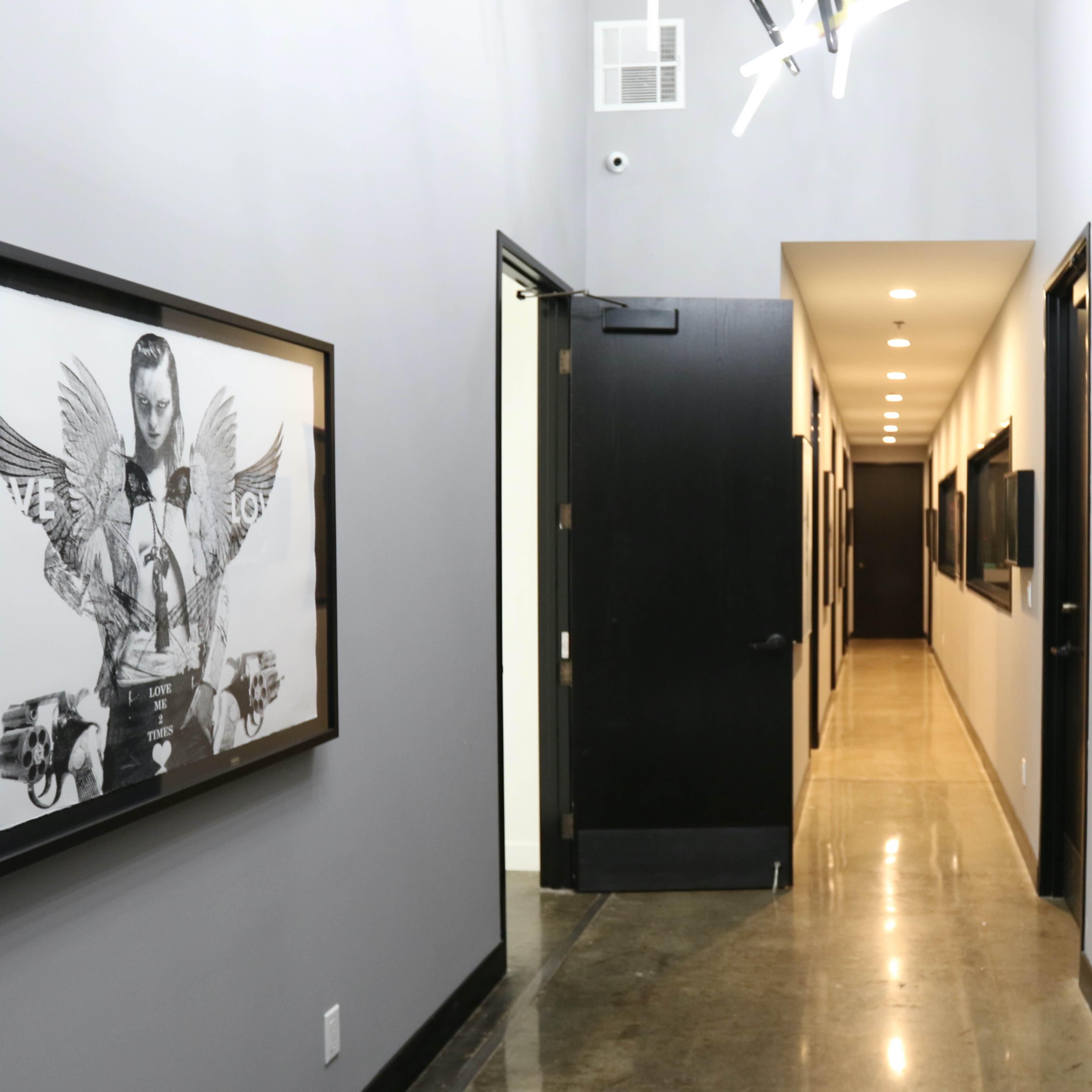 A long hallway with gray walls features framed artwork on one side and several doors leading to other rooms.
