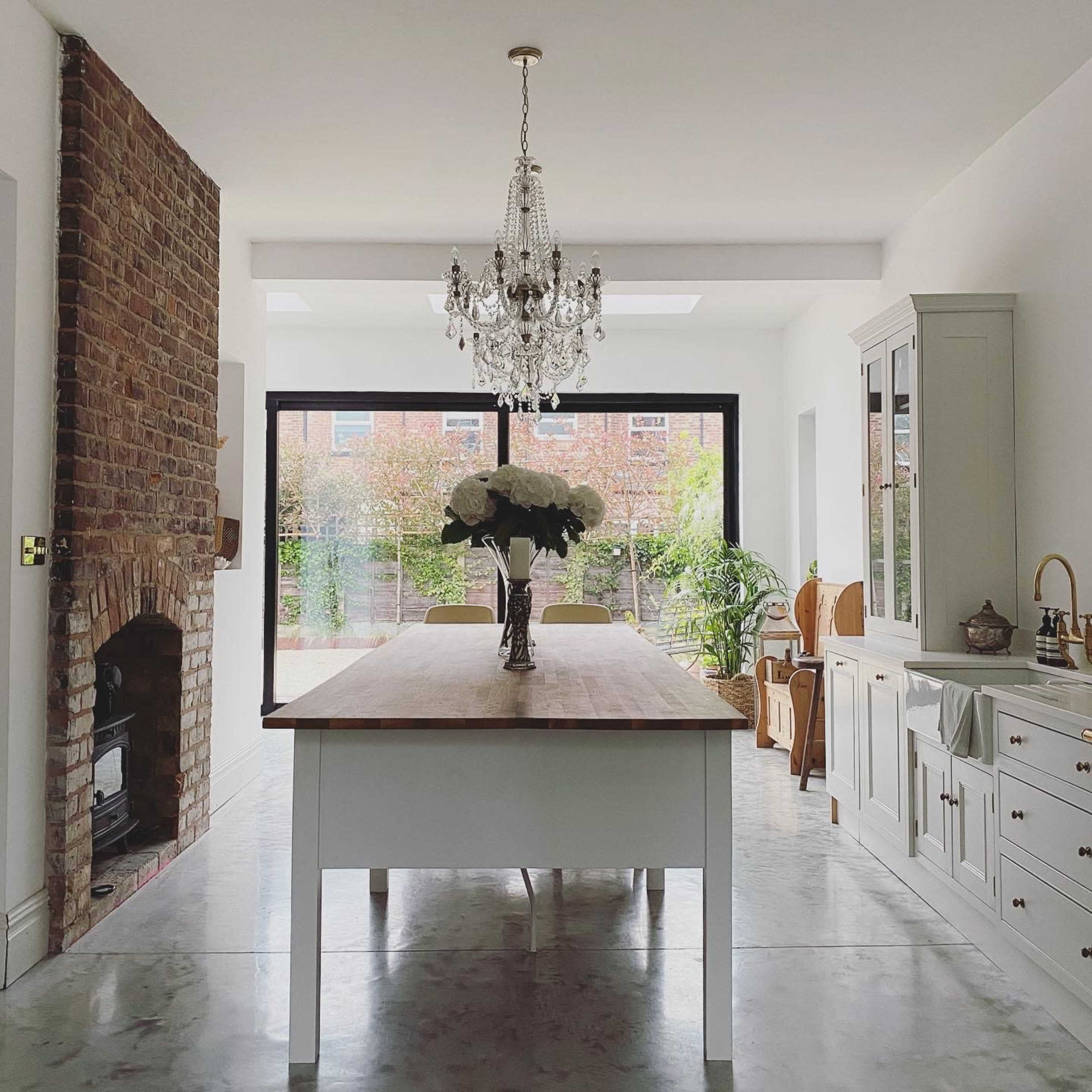 A modern dining area features a wooden table, a chandelier, and large windows overlooking a garden.