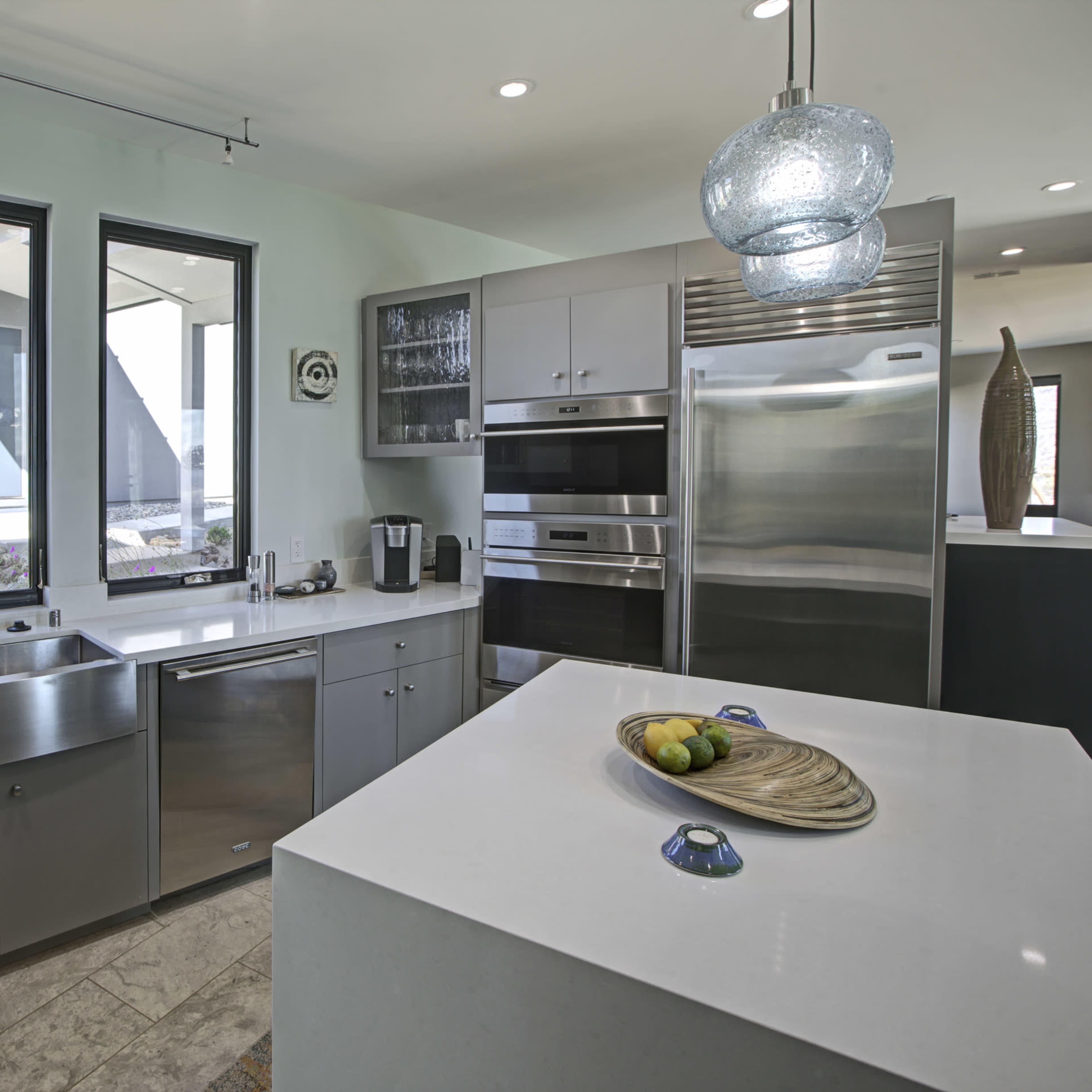 The kitchen features stainless steel appliances, white countertops, and large windows that provide ample natural light.