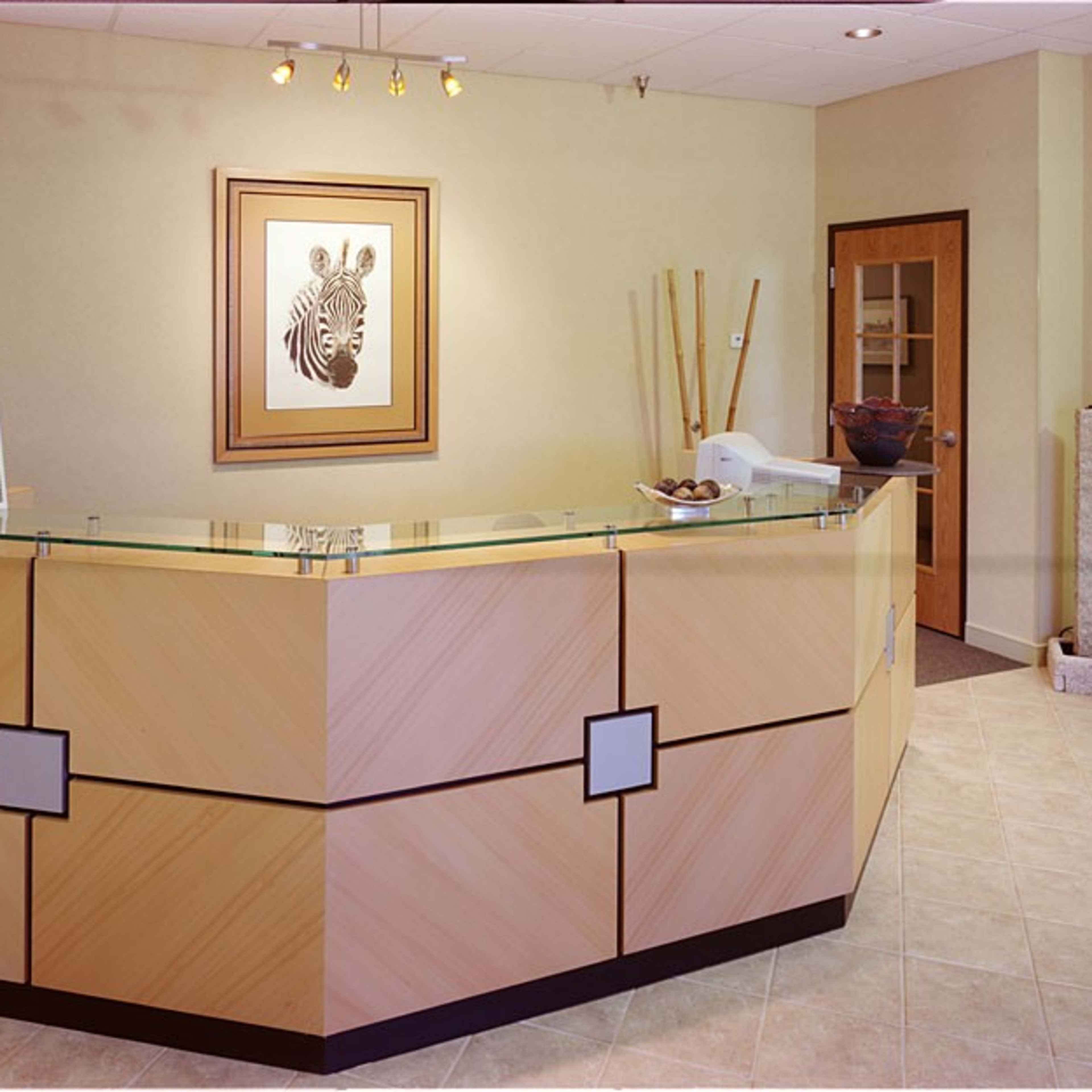 A reception area with a wooden front desk, a zebra artwork on the wall, and potted plants in the corner.