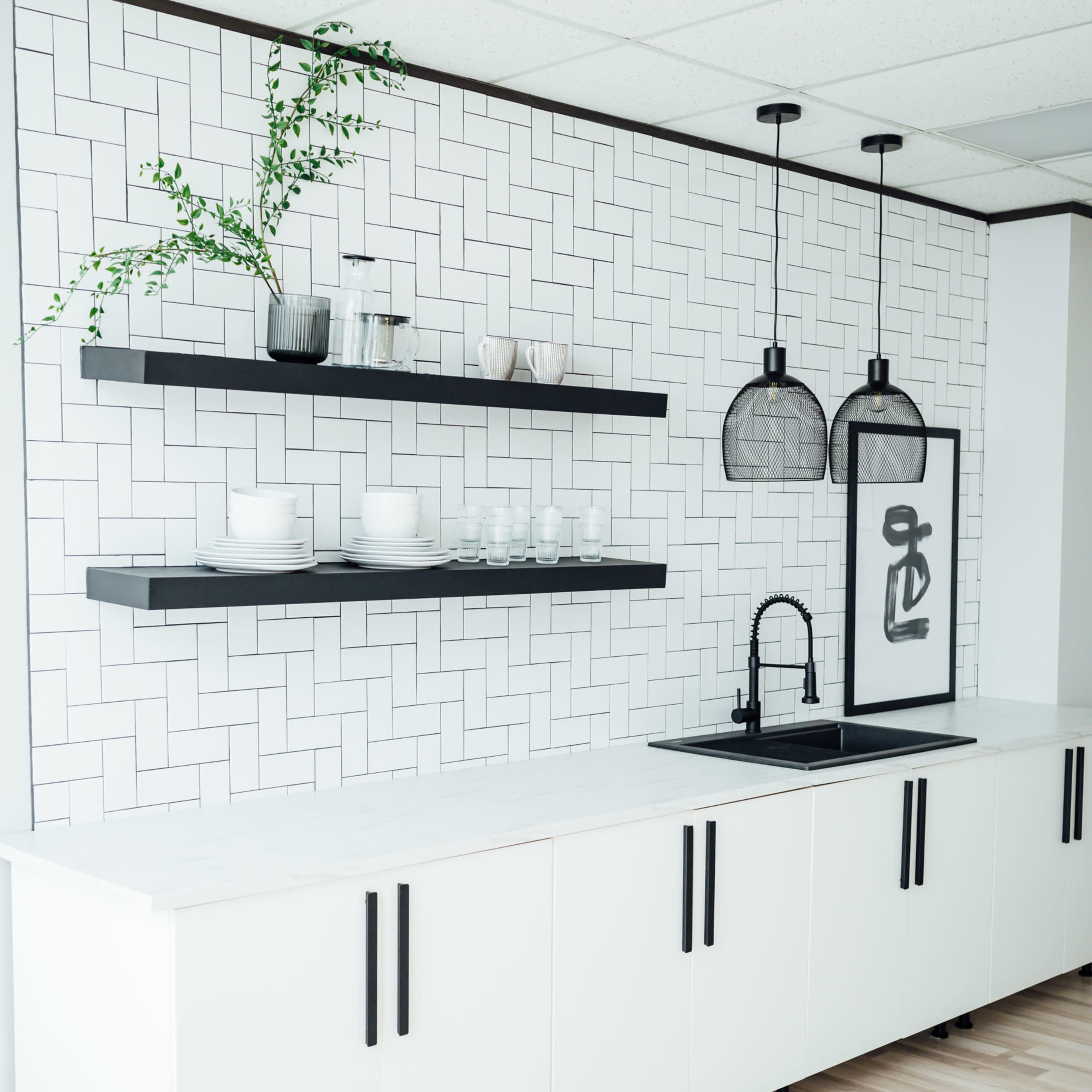 A modern kitchen setup featuring white cabinetry, black shelving, and pendant lights above a sink area, all against a textured white tile wall.