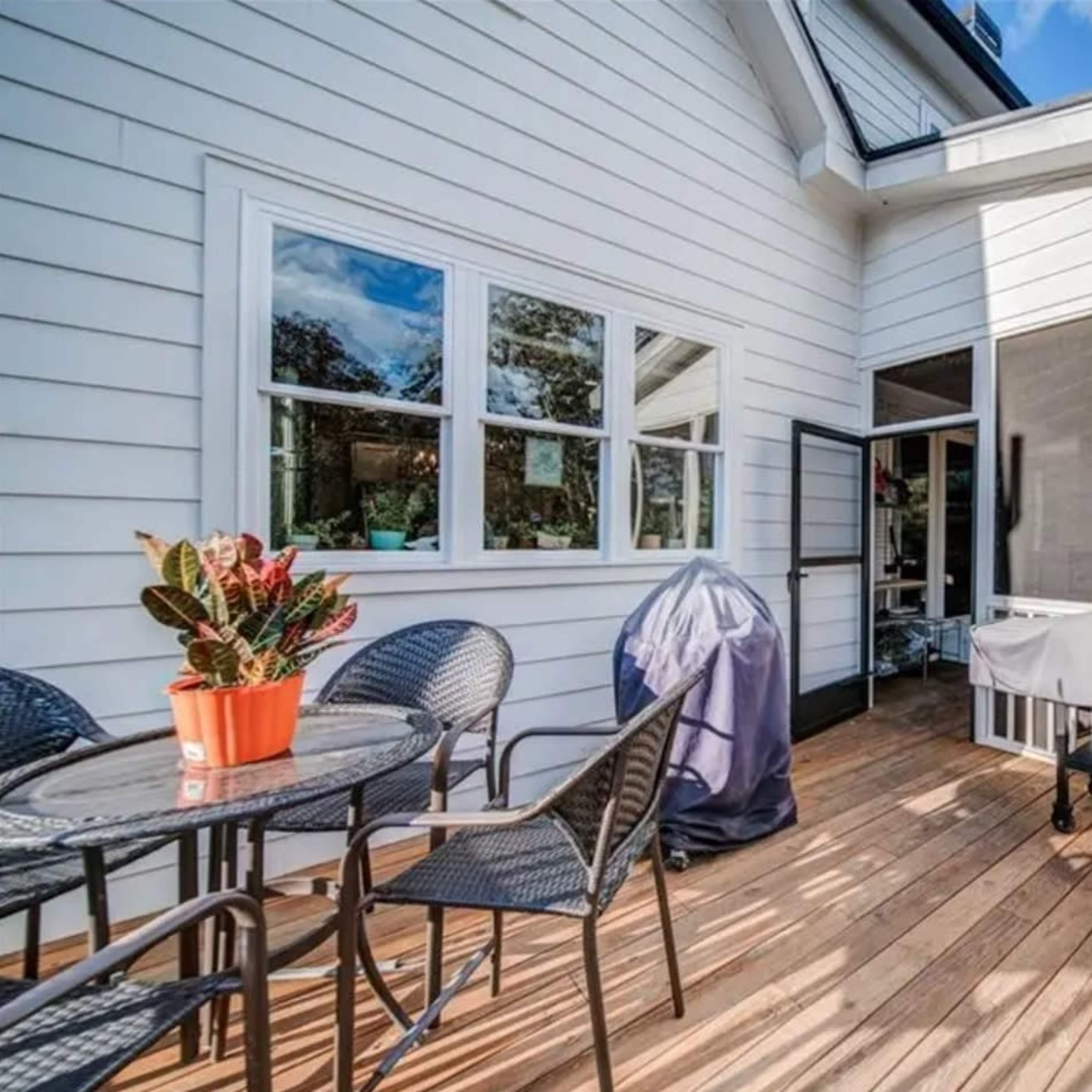 A wooden deck with a table and chairs, a potted plant, and a covered grill near a screened-in area of a house.