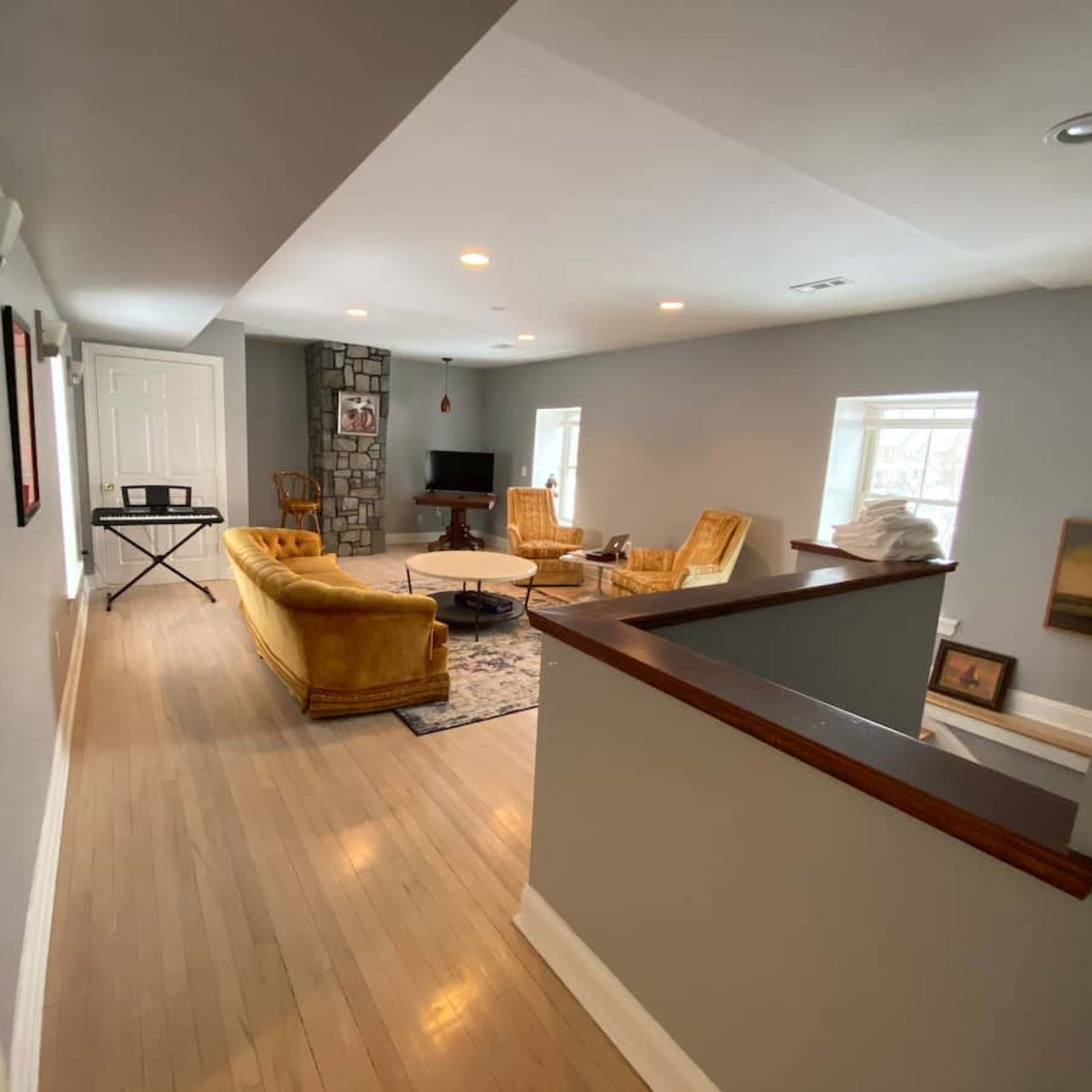 A hallway leads to a spacious living area featuring a yellow couch, two armchairs, and a stone fireplace.