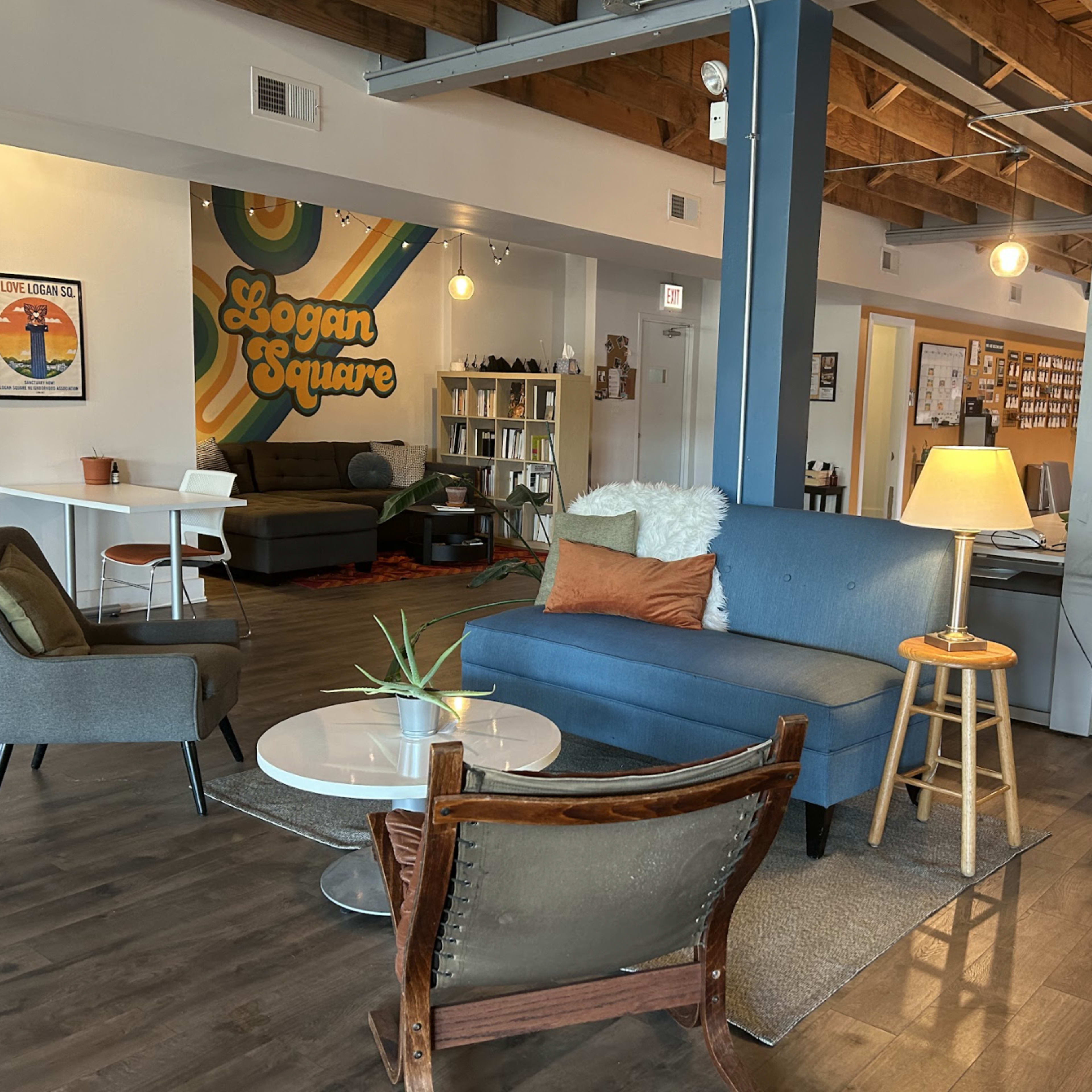 A modern workspace featuring a blue sofa, two armchairs, a coffee table, and a decorative wall with "Logan Square" written on it.