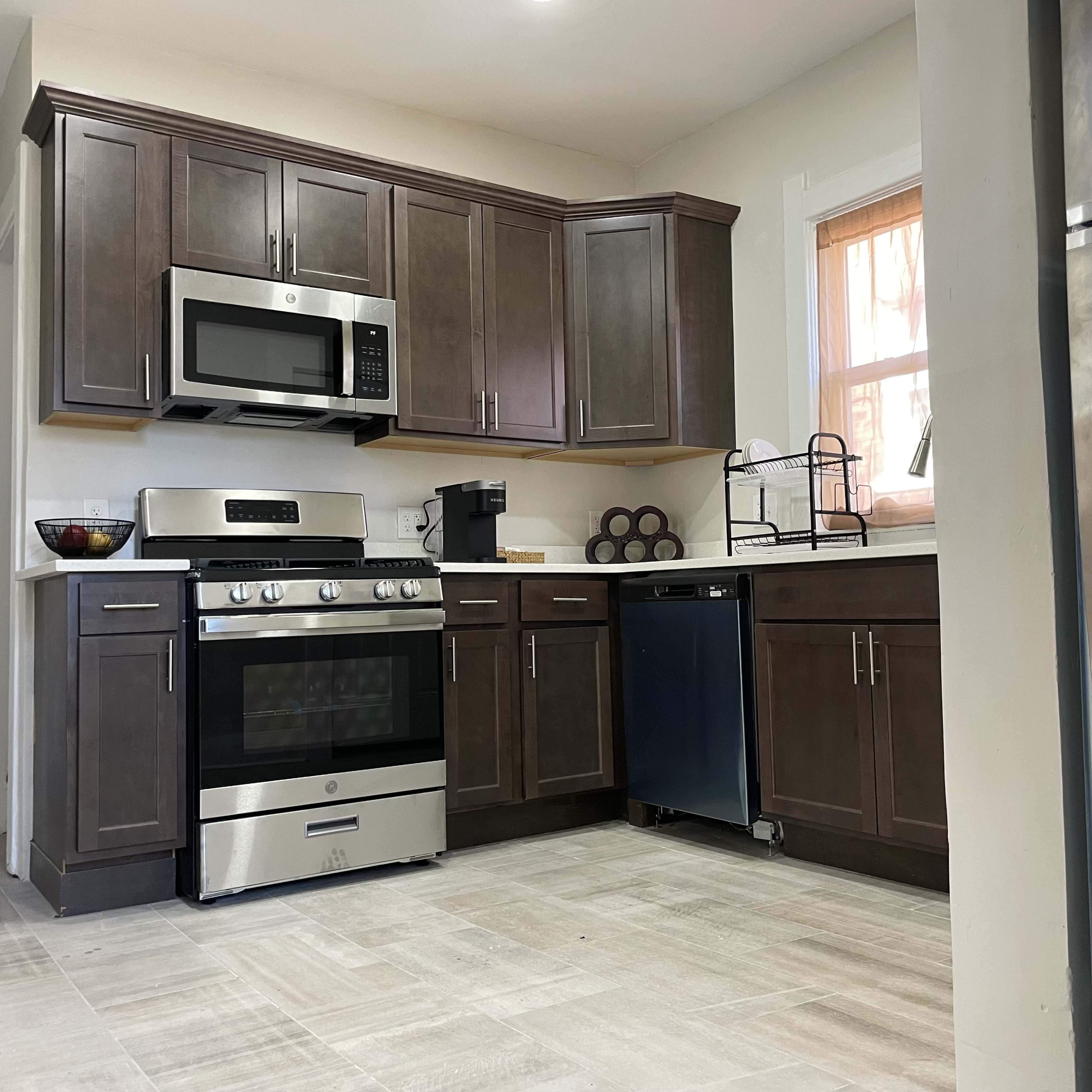 A modern kitchen with dark wood cabinets, a stainless steel stove and microwave, and a silver dishwasher.
