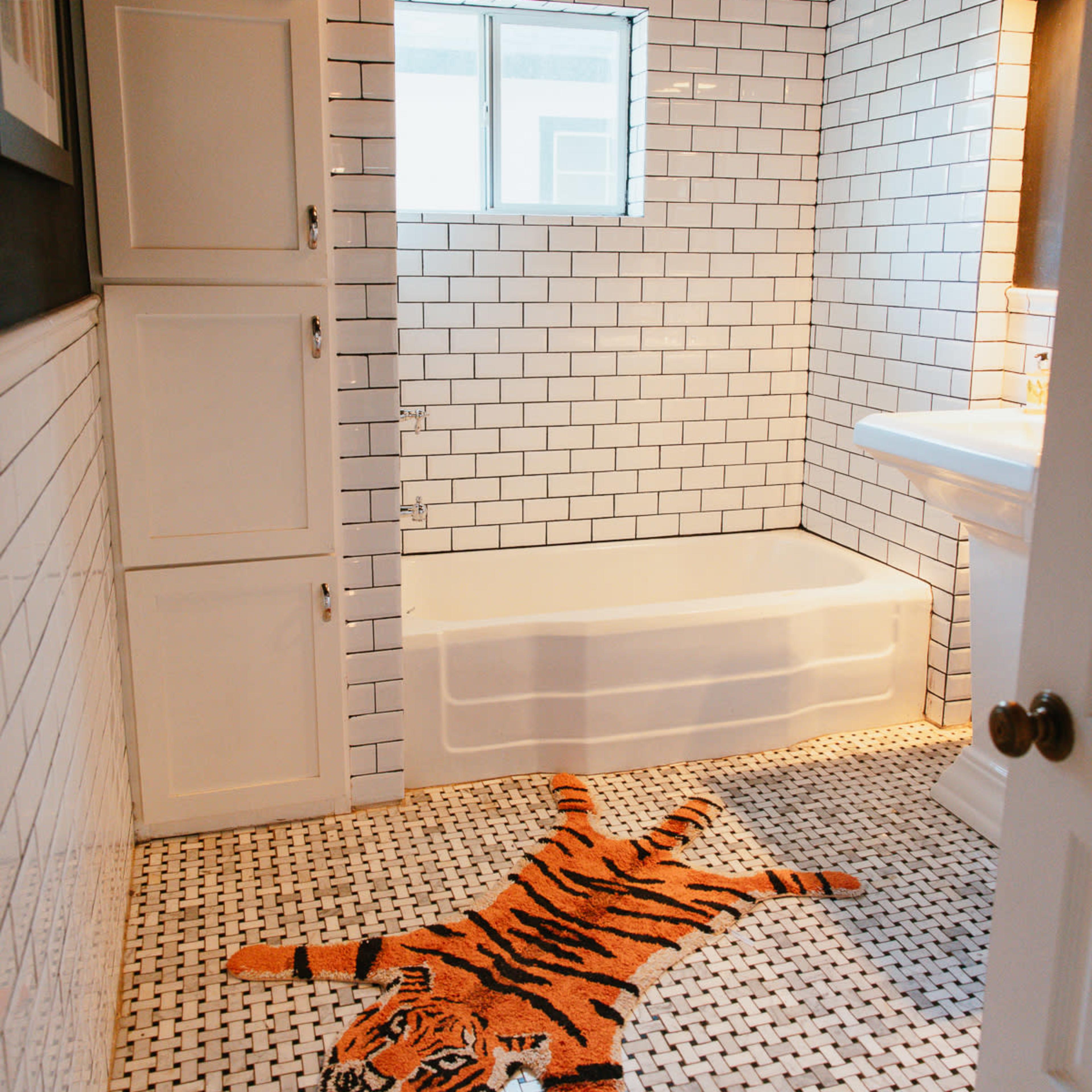 The bathroom features white subway tile walls, a bathtub, and a tiger-shaped bath mat on the tiled floor.