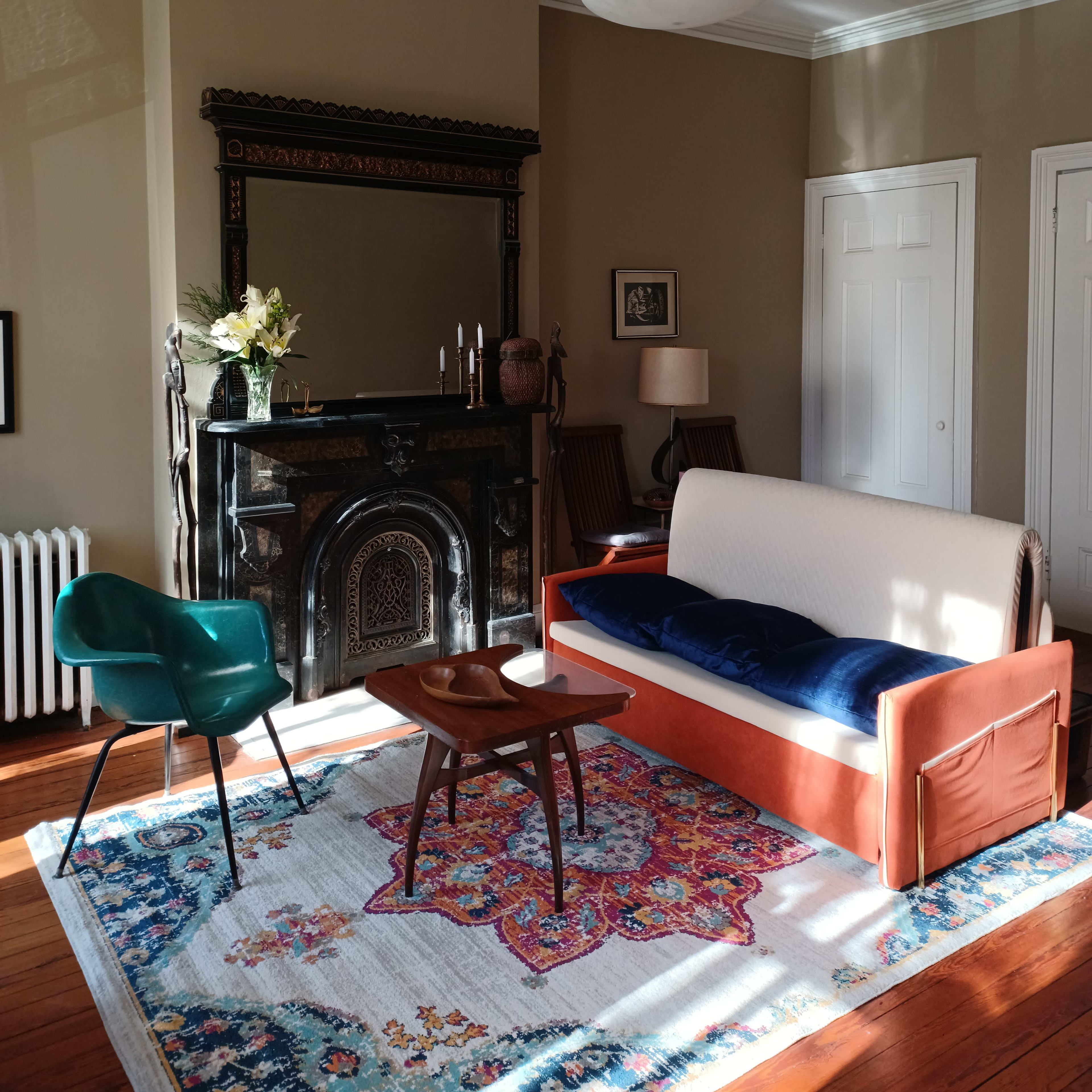 A living room features a sofa, a wooden coffee table, a patterned rug, and a decorative fireplace with a mirror above it.