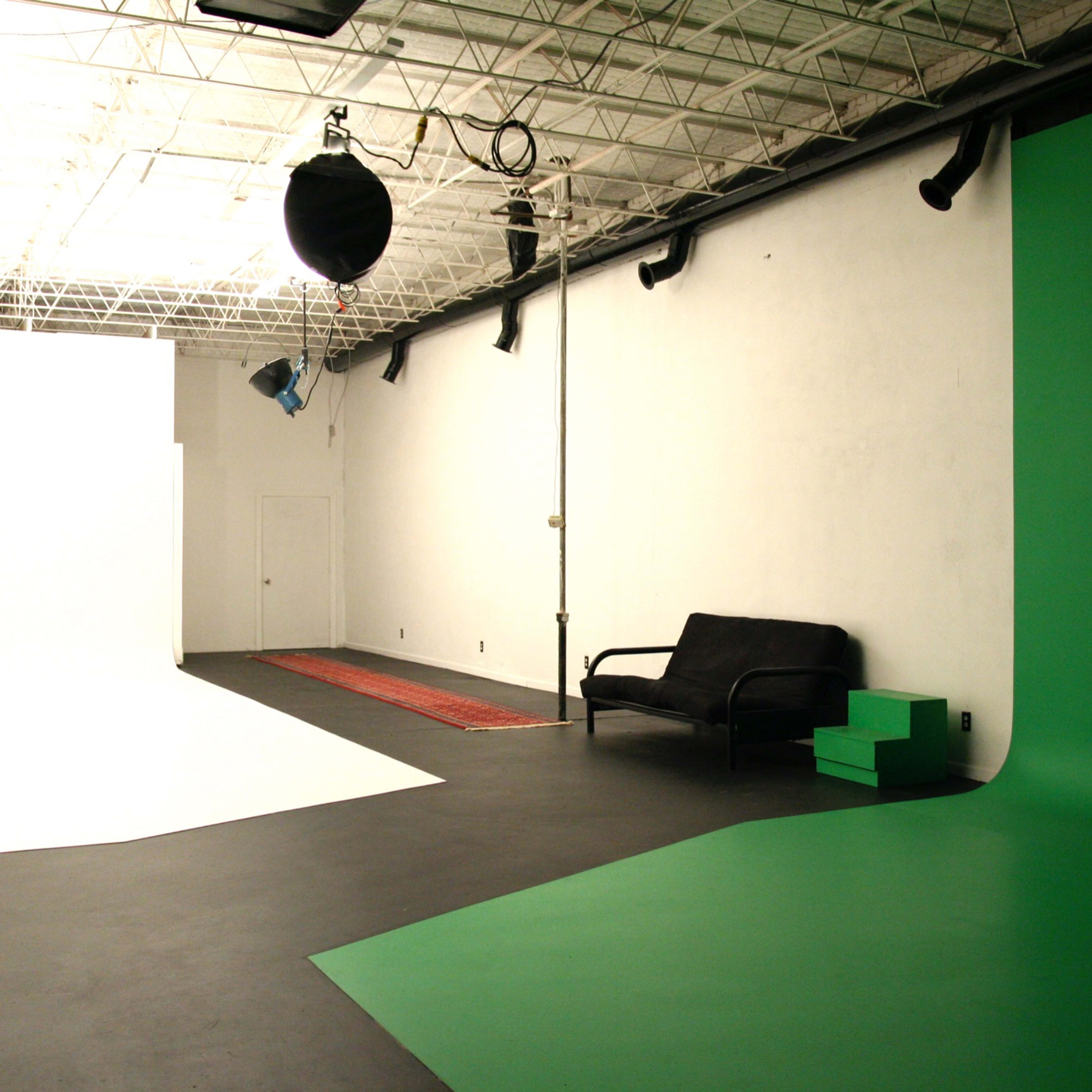 A photography studio with a white backdrop, a green backdrop, a black sofa, and a desk with a chair.
