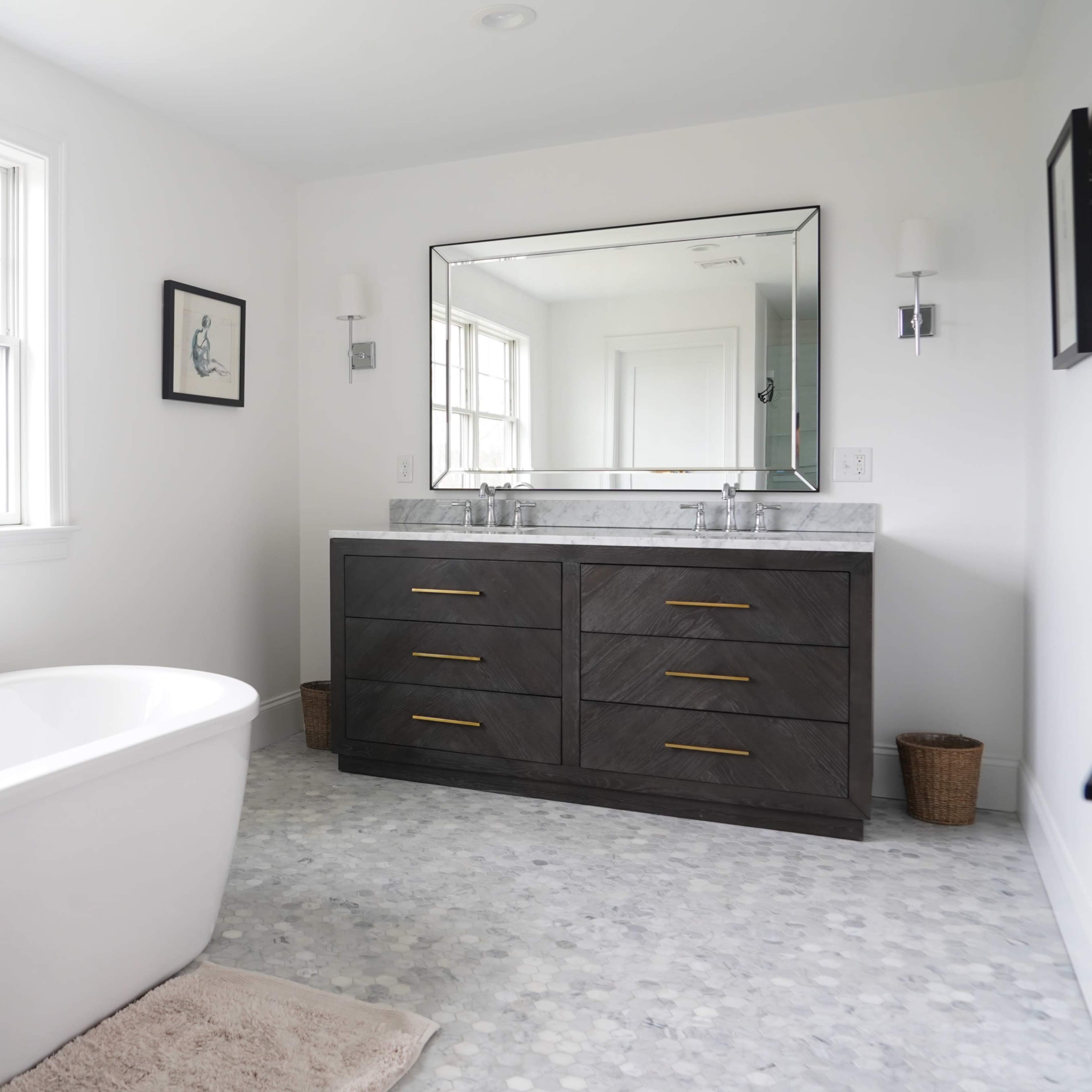 The bathroom features a freestanding white bathtub next to a dark wooden double vanity with a large mirror and two sinks, set against a backdrop of large windows.